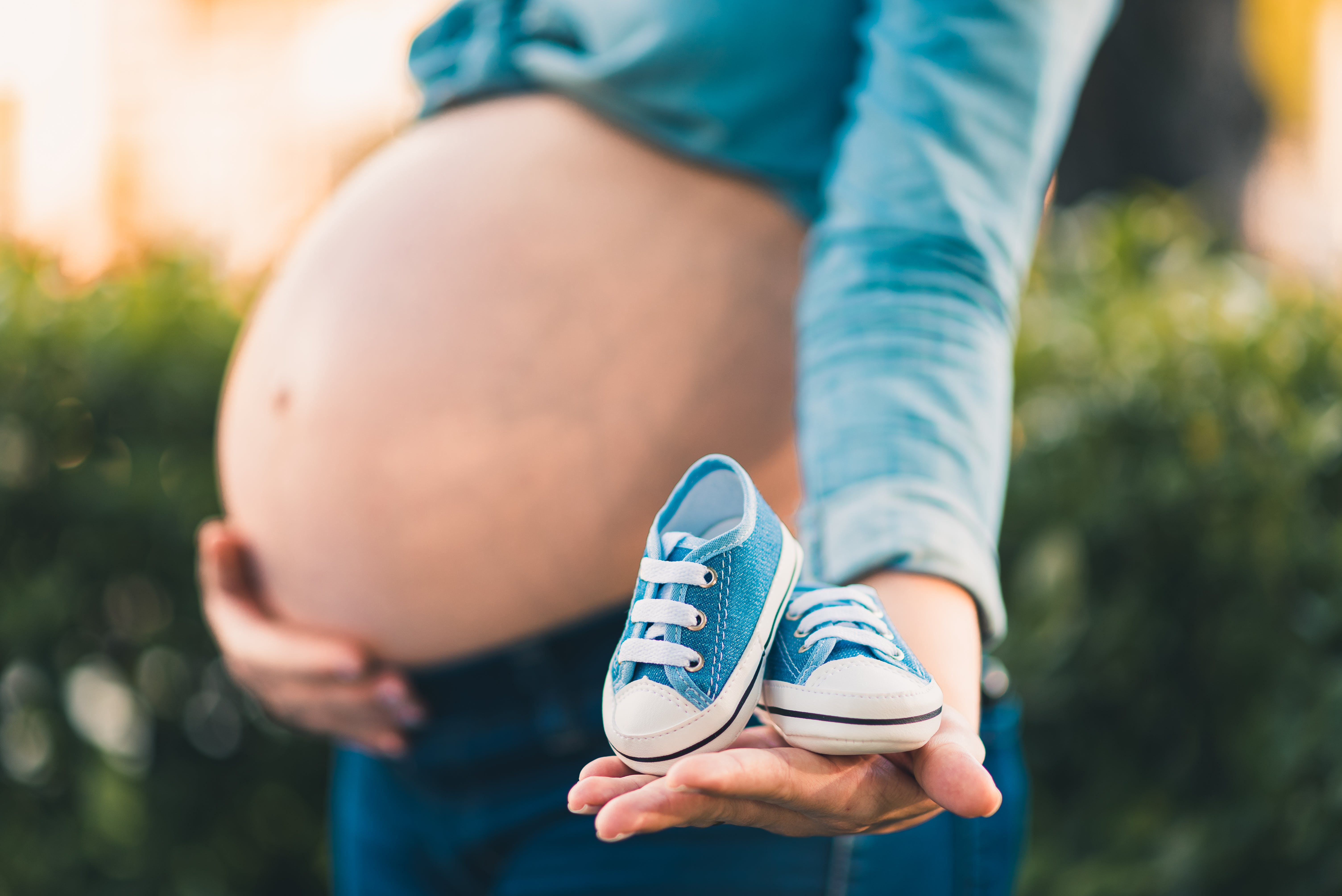 Une femme enceinte tenant son ventre dans une main et une paire de baskets bleues pour bébé dans l'autre | Source : Pexels