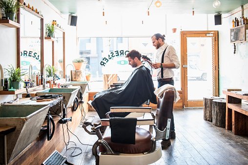 Un styliste caucasien coupe les cheveux d'un client chez le coiffeur. | Photo : Getty Images