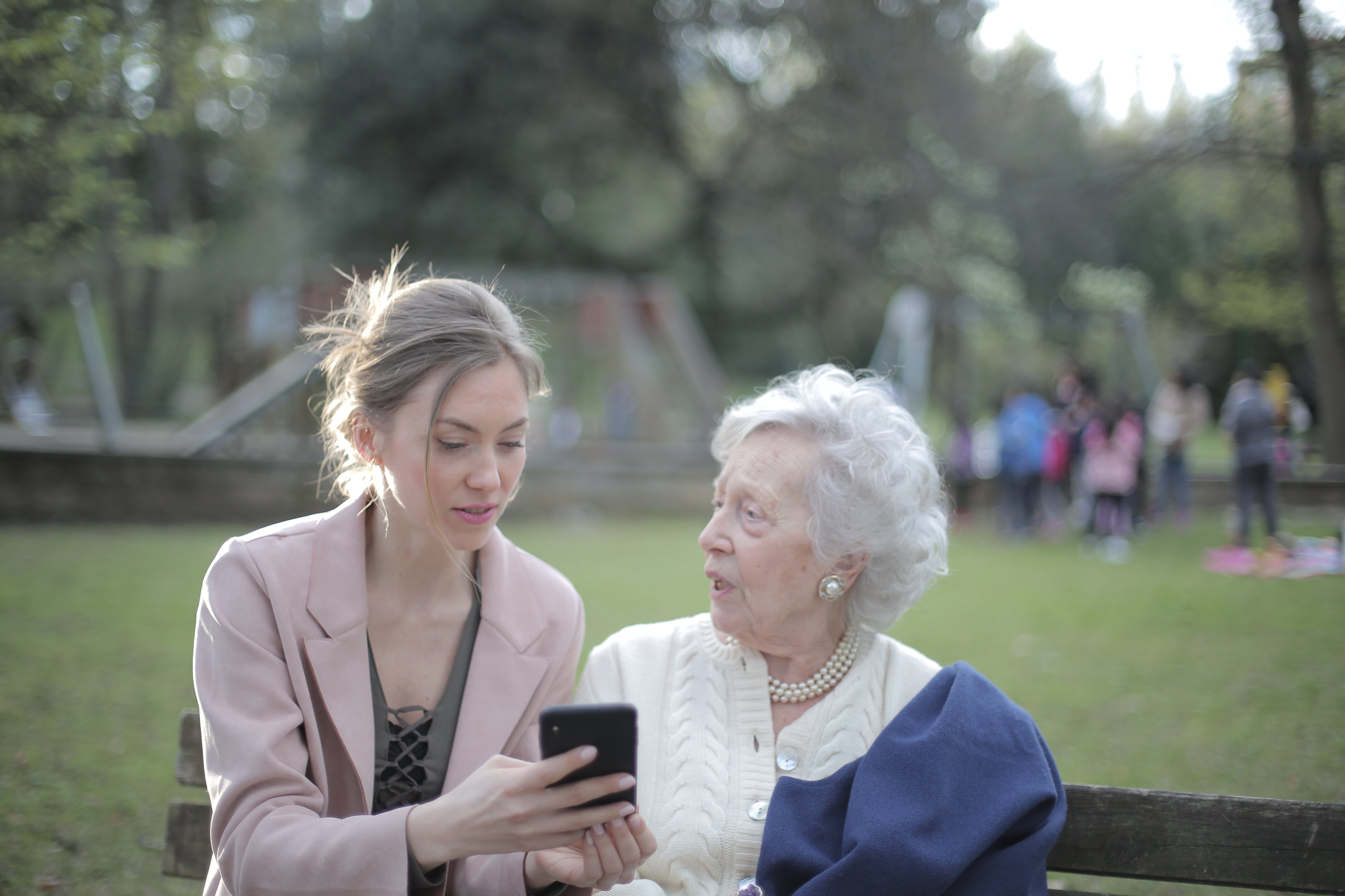 Une femme plus jeune montre à une plus âgée quelque chose sur son téléphone alors qu'elle se trouve à l'extérieur | Source : Pexels