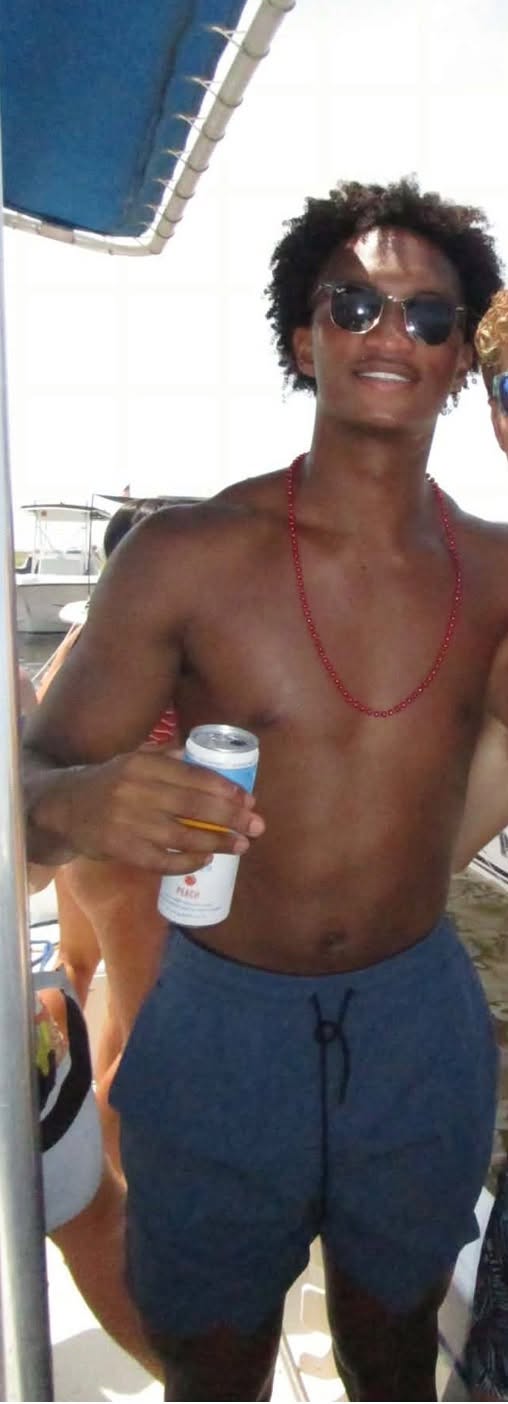 Nolan Wells sourit, un verre à la main, sur le bateau pendant les festivités du 4 juillet. Il a passé l'après-midi en maillot de bain bleu, lunettes de soleil et collier de perles rouges. | Source : Facebook/christine.wonsley