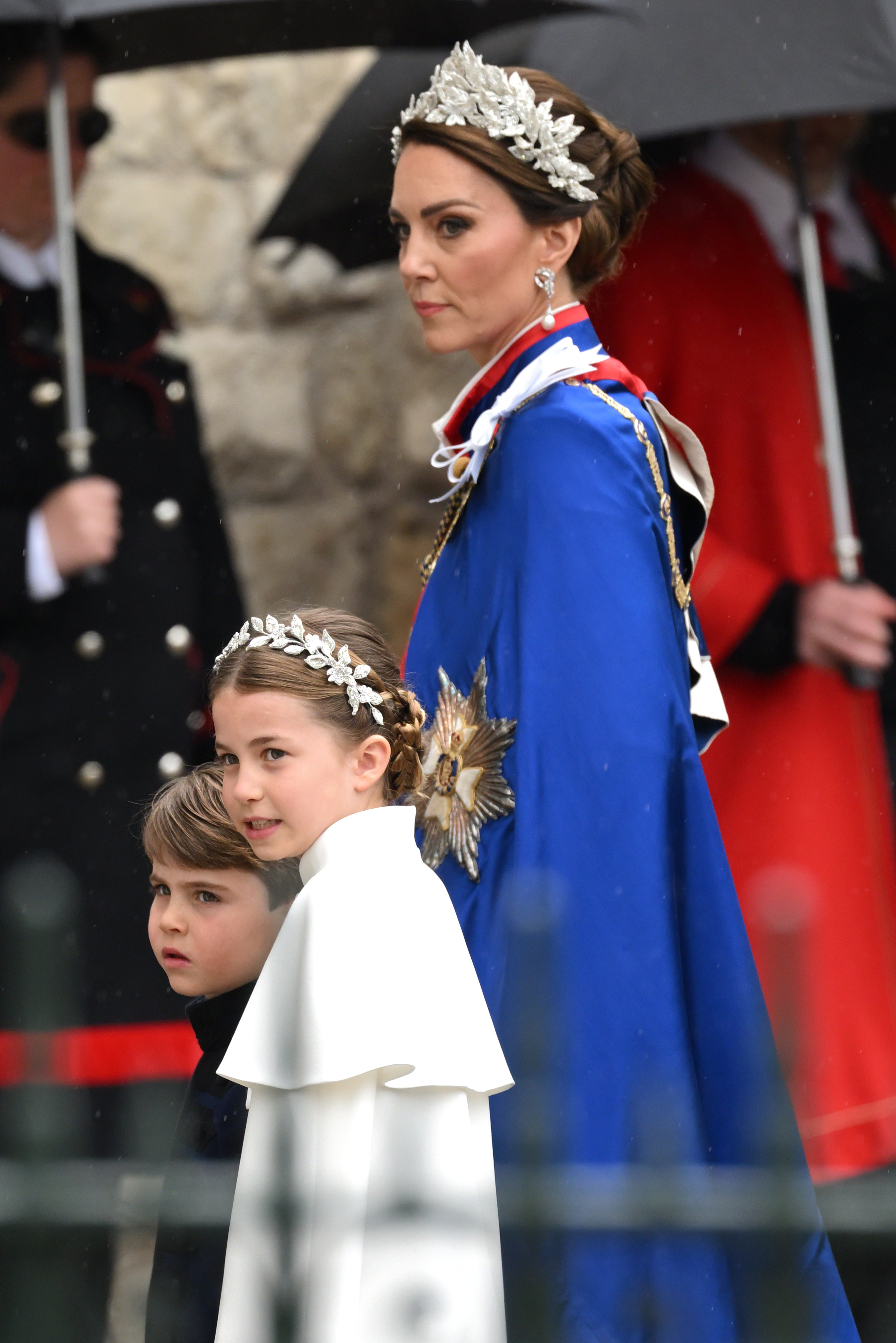 La princesse Charlotte arrive aux côtés du prince Louis et de Catherine, princesse de Galles, à l'abbaye de Westminster pour le couronnement du roi Charles III et de la reine Camilla, le 6 mai 2023, à Londres, en Angleterre. Charlotte ressemble à sa mère dans une robe Alexander McQueen ivoire avec une cape et une coiffe sophistiquée ornée de fils d'argent et de fleurs en cristal, marchant aux côtés du prince Louis qui porte une tunique bleu marine Dege & Skinner, tandis que Catherine se tient majestueusement dans son manteau de l'Ordre royal victorien et une coiffe fleurie assortie. | Source : Getty Images