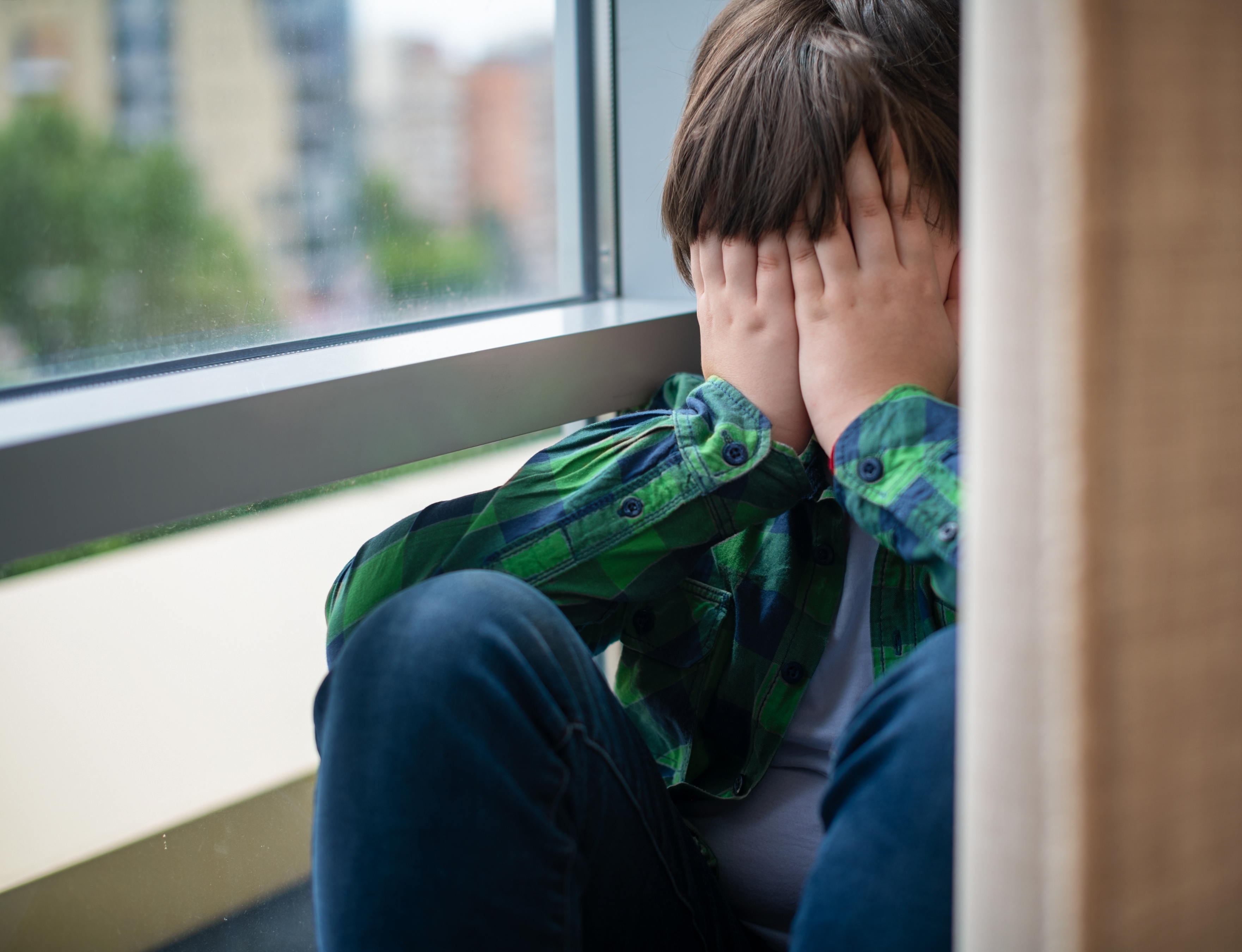 Un jeune garçon se cachant le visage près d'une fenêtre. | Source : Shutterstock