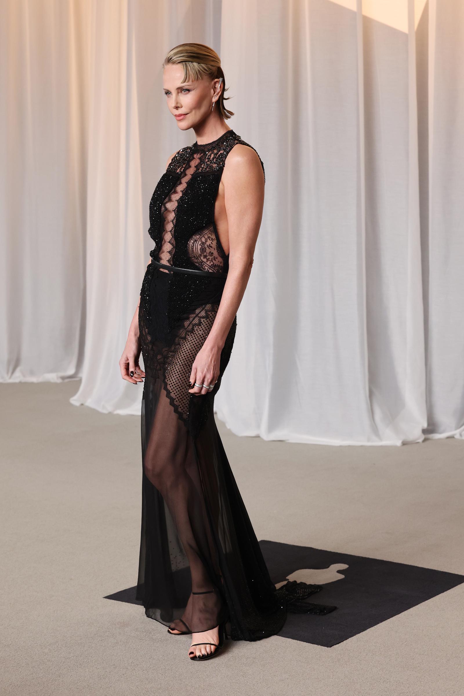 Charlize Theron fait sensation sur le tapis rouge dans une robe noire transparente sans manches, richement ornée de dentelle délicate, de perles et d'empiècements en résille. Mise en valeur par une ceinture fine à la taille et accompagnée d’un chignon lisse effet mouillé ainsi que de sandales noires minimalistes, la lauréate d’un Oscar allie un glamour moderne et audacieux à l’élégance classique d’une star de cinéma alors qu’elle célèbre la remise de son Icon Award.