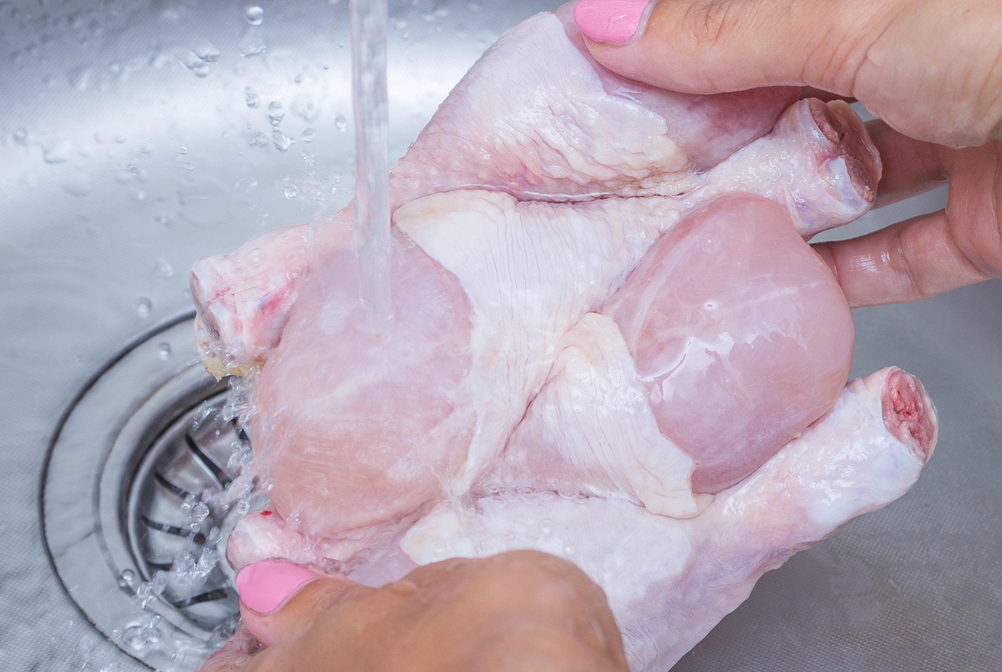 Femme qui lave un poulet cru congelé. | Photo : Getty Images