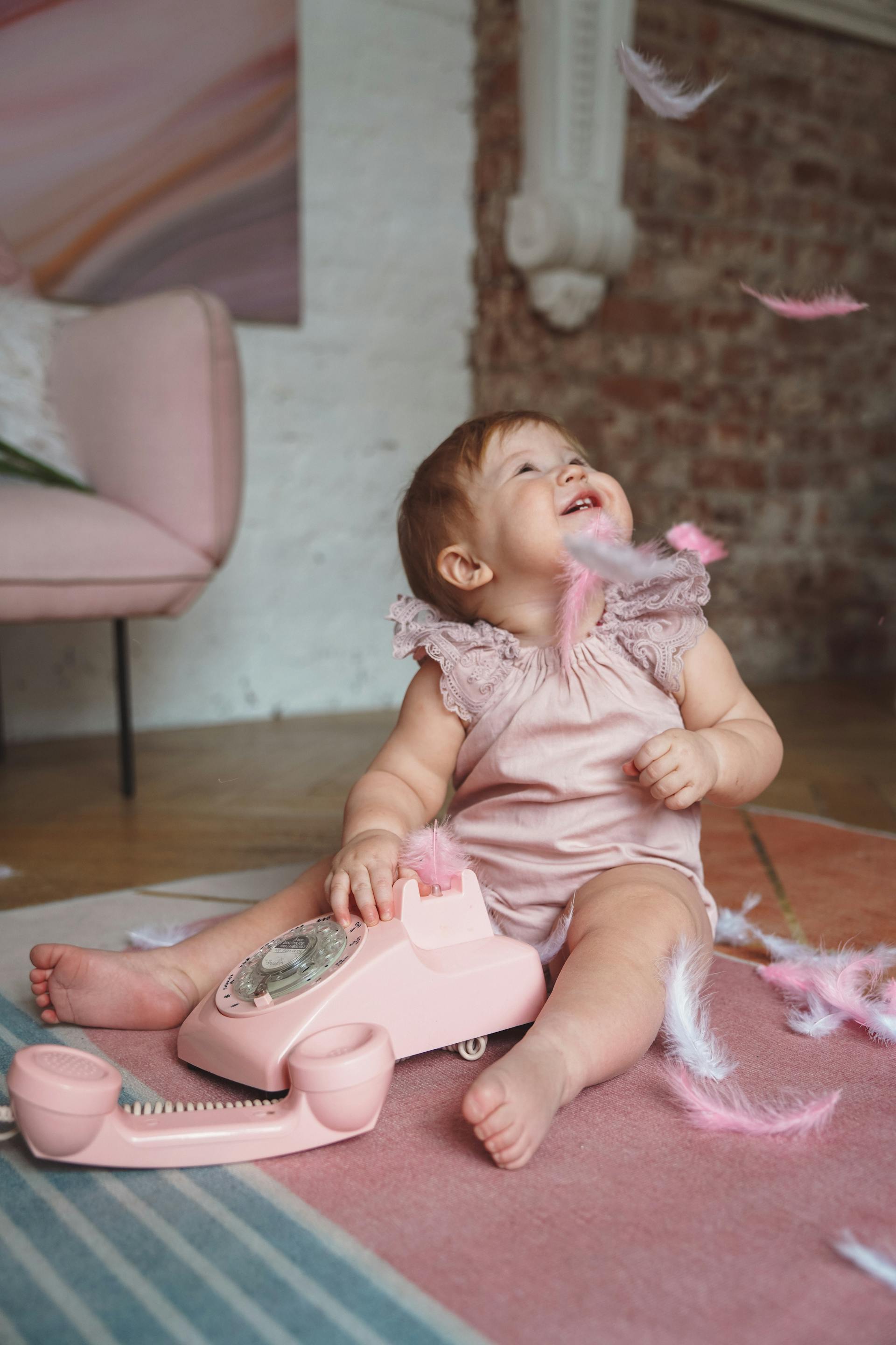 Une petite fille habillée en rose qui joue avec des plumes et un téléphone rose.