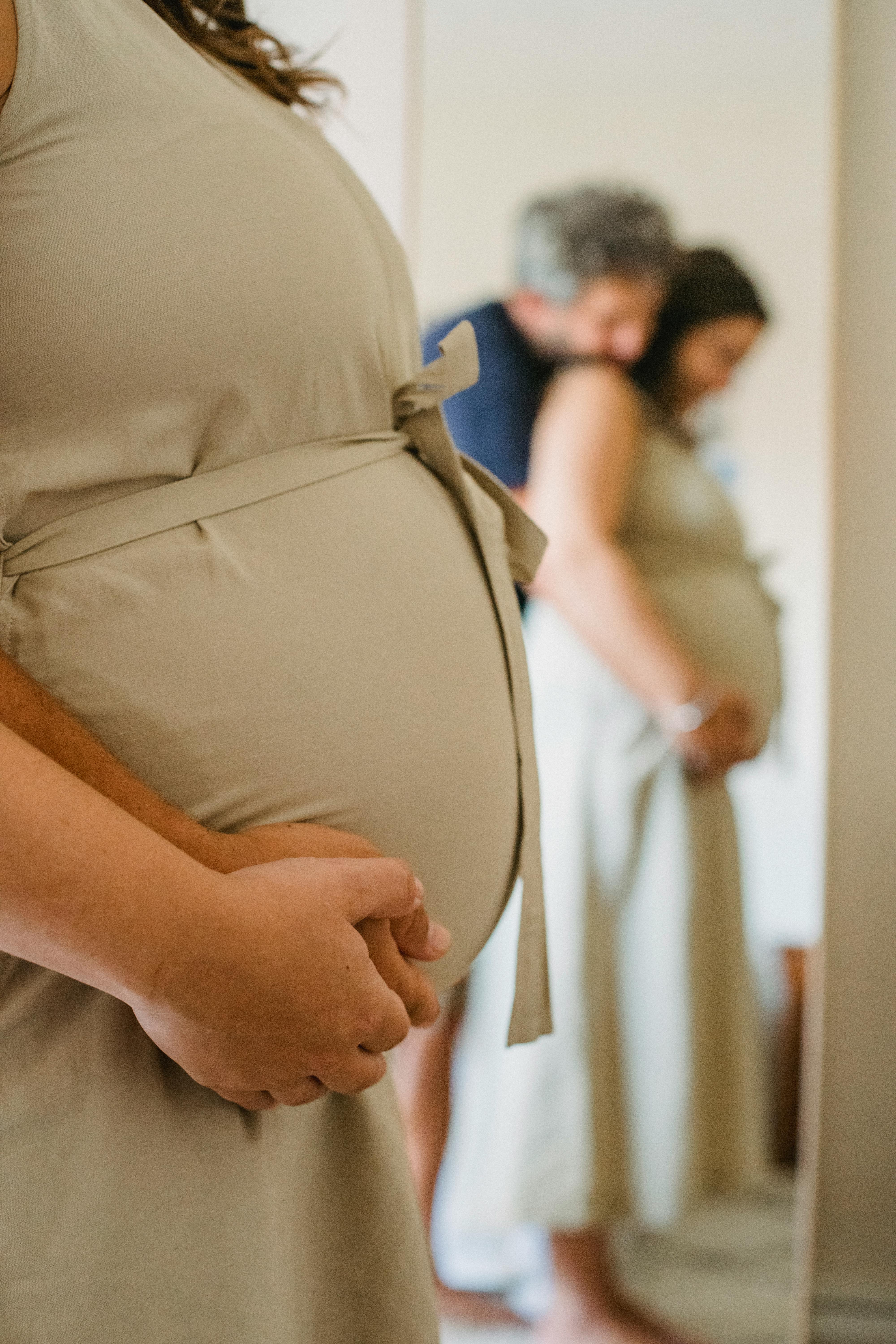 Un mari et sa femme enceinte s'embrassant devant un miroir | Source : Pexels
