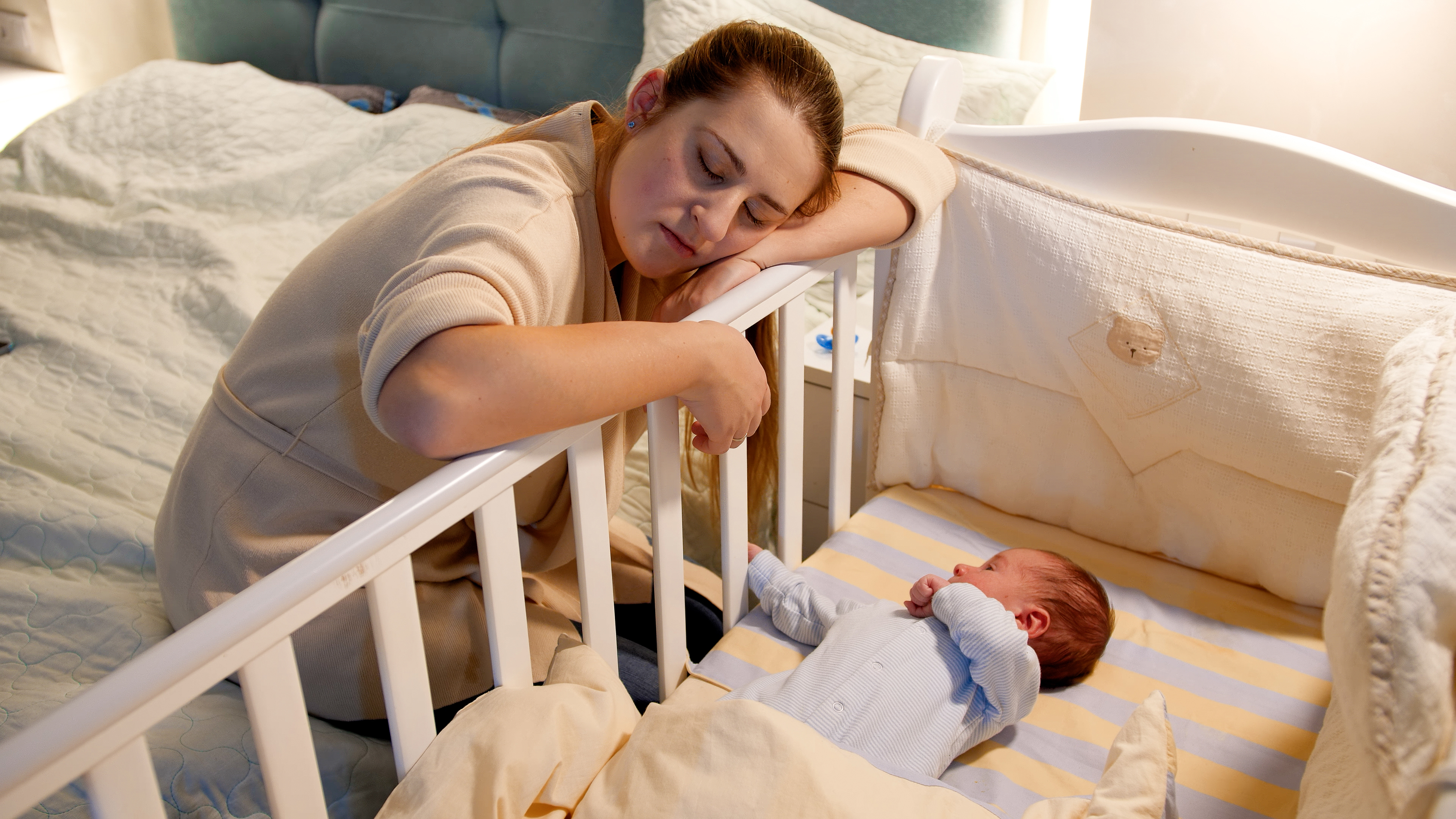 Mère fatiguée dormant près du berceau de son enfant | Source : Shutterstock