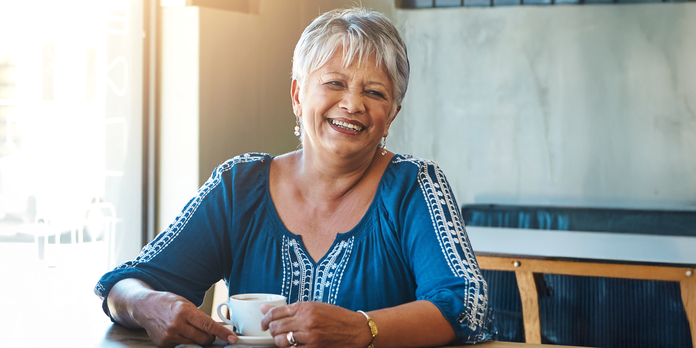 Une femme âgée ravie, aux cheveux gris courts, assise à une table | Source : Shutterstock