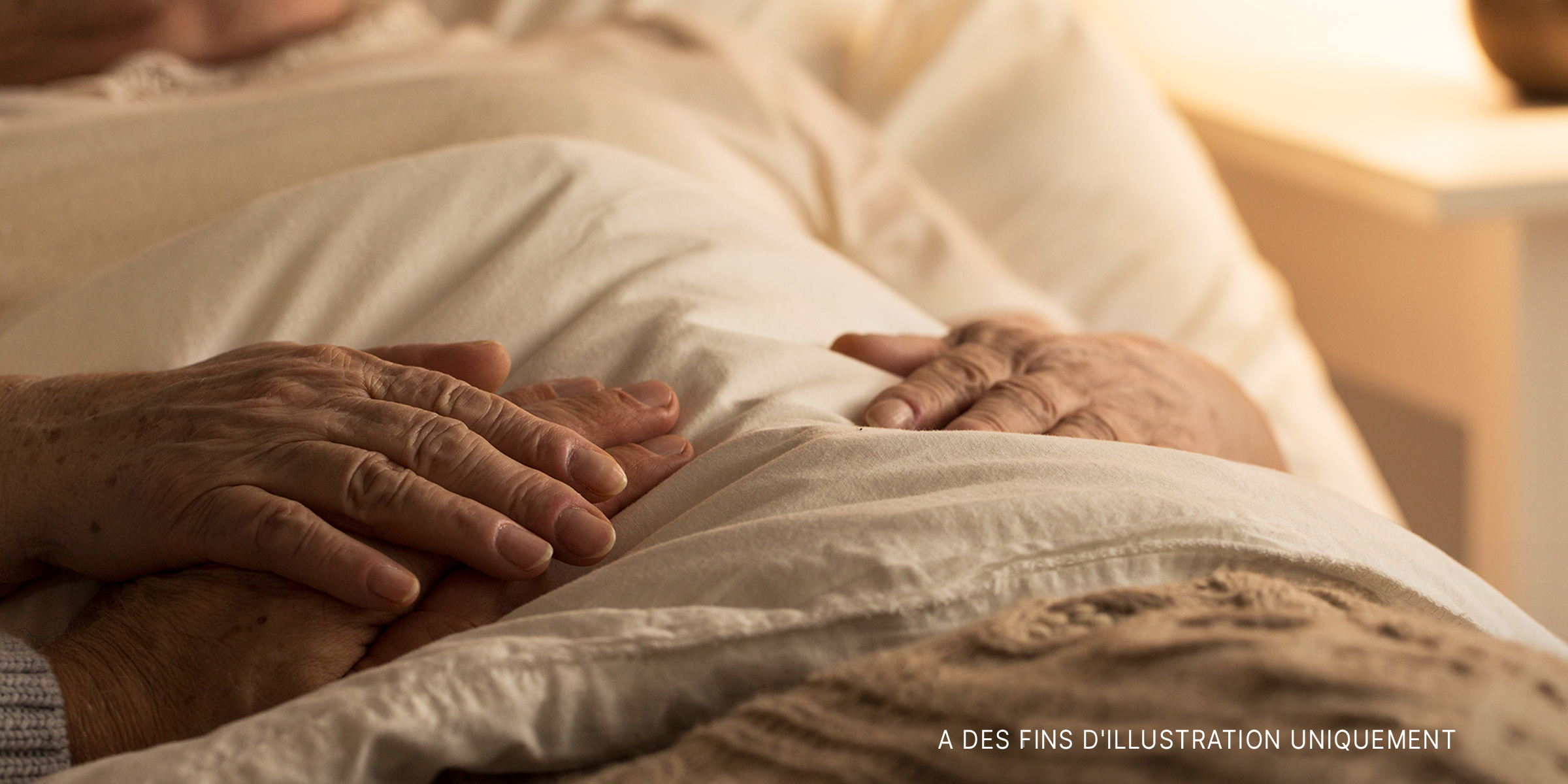 Mains reposant sur le dessus des couvertures dans un lit d'hôpital | Source : Getty Images