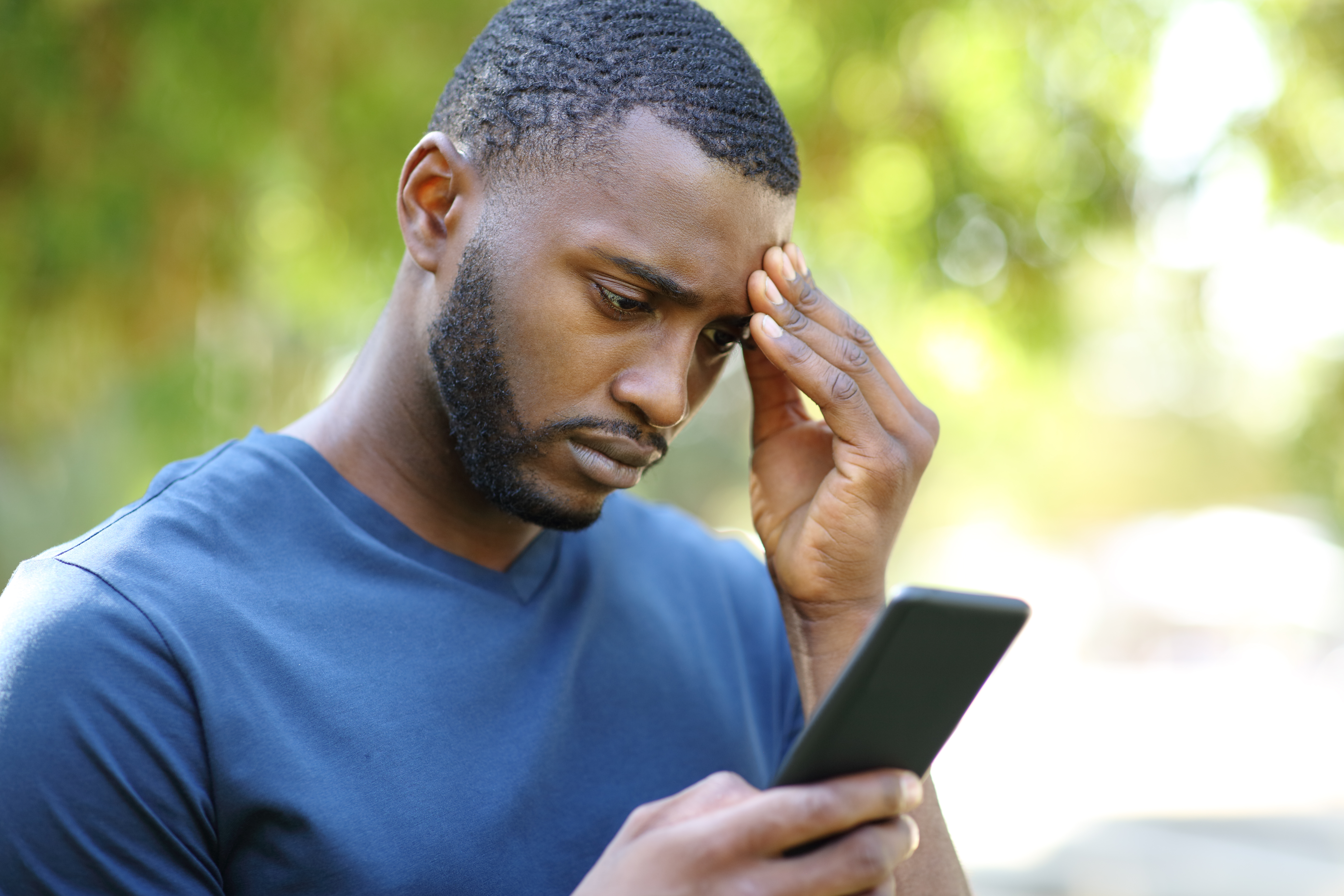 Un homme noir inquiet consulte son smartphone dans un parc | Source : Getty Images
