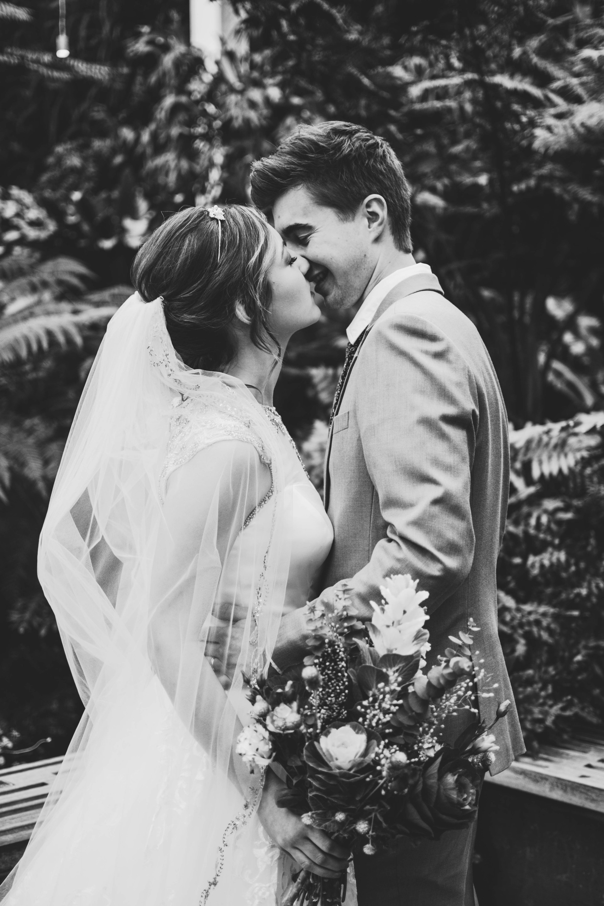 Photo en niveaux de gris d'un couple de jeunes mariés qui verrouille ses lèvres | Source : Unsplash