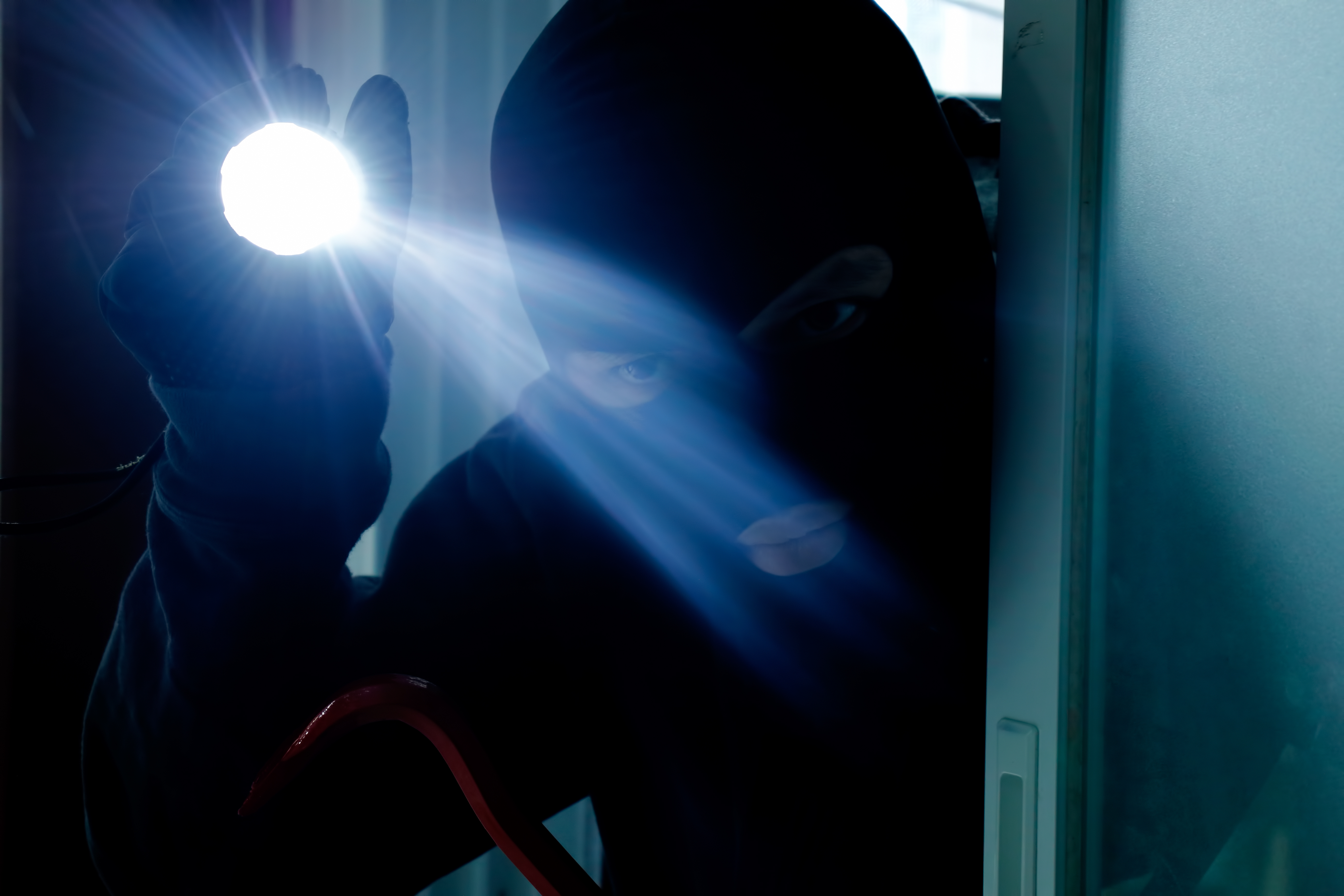 Un cambrioleur cagoulé tient une lampe de poche tout en entrant secrètement dans une maison | Source : Getty Images