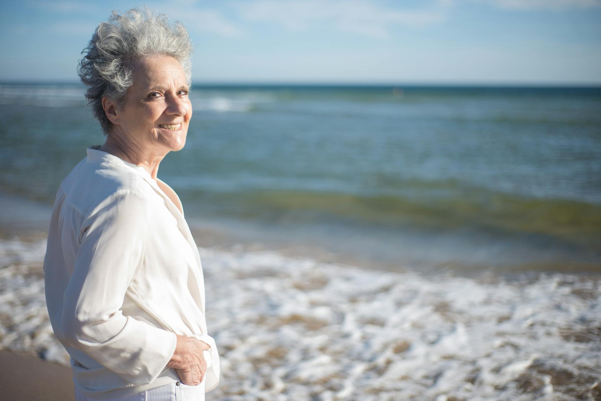 Une femme âgée sourit en se tenant au bord de la mer | Source : Pexels