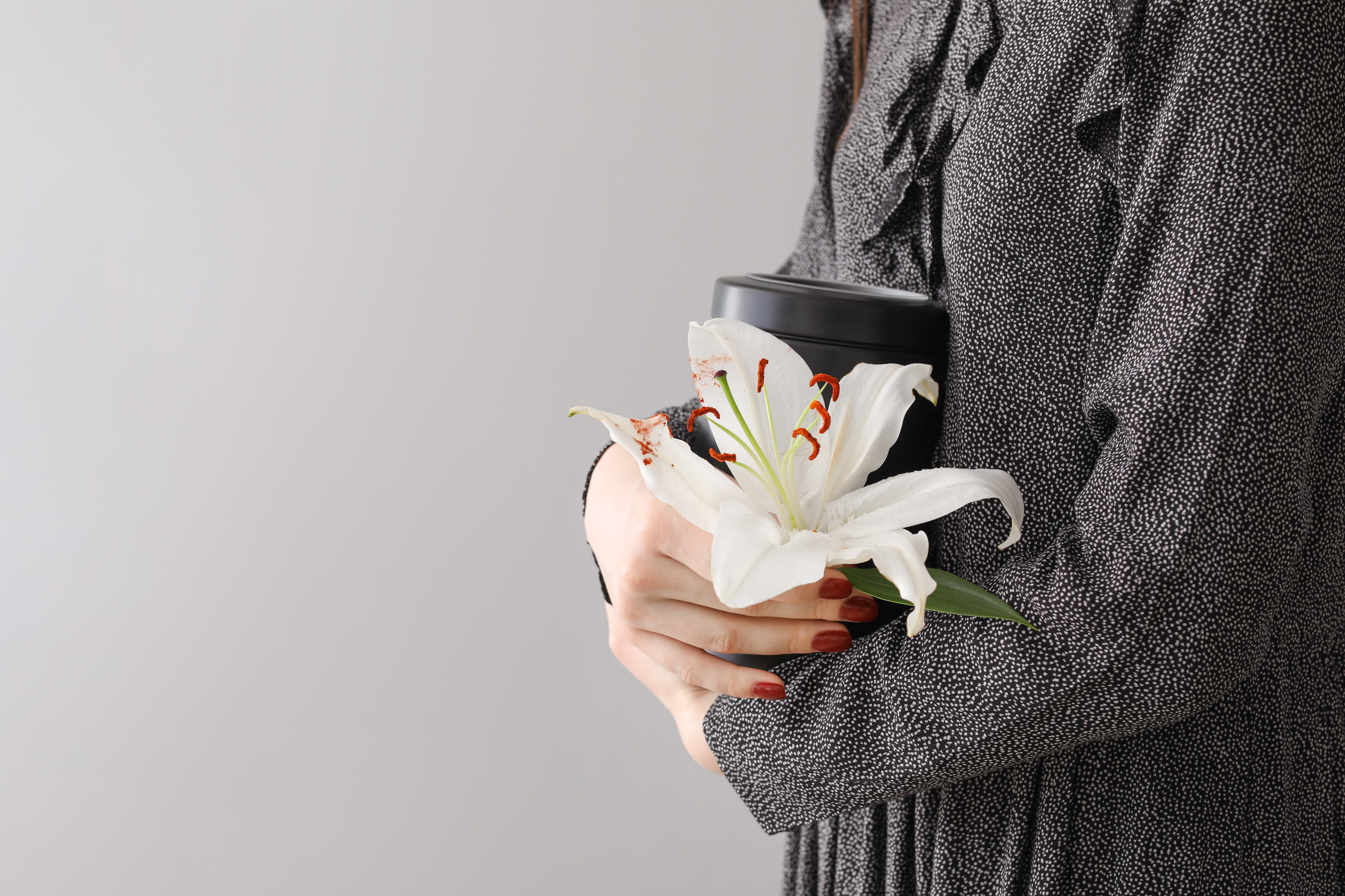 On voit une femme tenant une urne mortuaire et une fleur de lys blanc | Source : Shutterstock