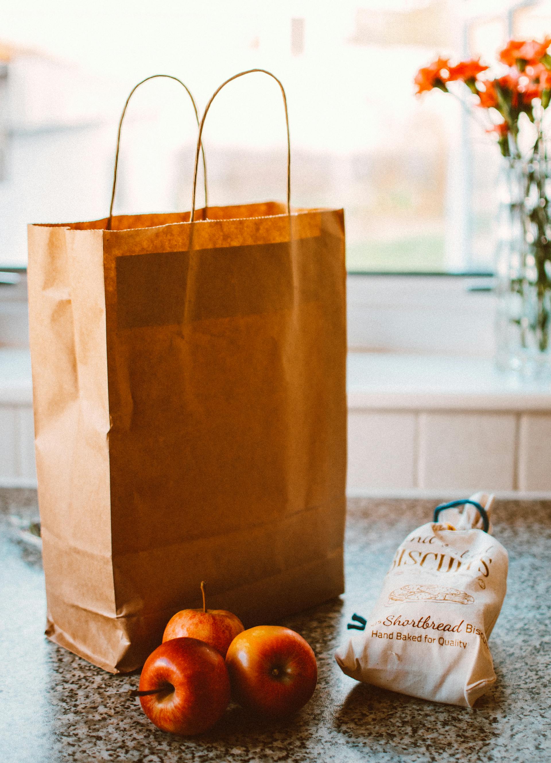 Plusieurs pommes posées à côté d'un sac en papier brun et d'un paquet de pain | Source : Pexels