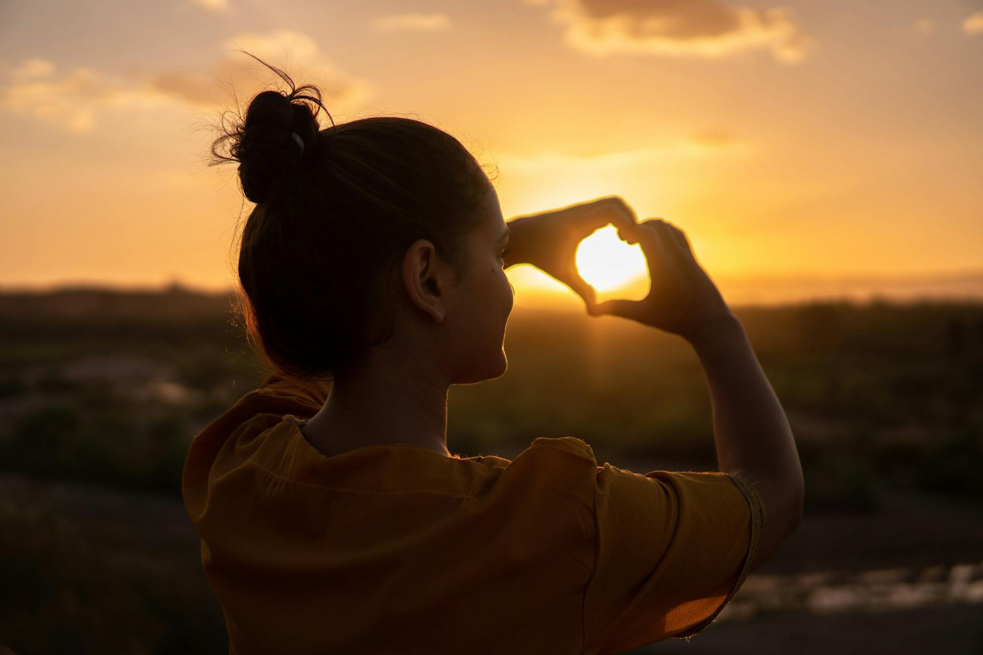 Vue de dos d'une femme faisant un signe de cœur avec ses mains à l'heure dorée | Source : Pexels