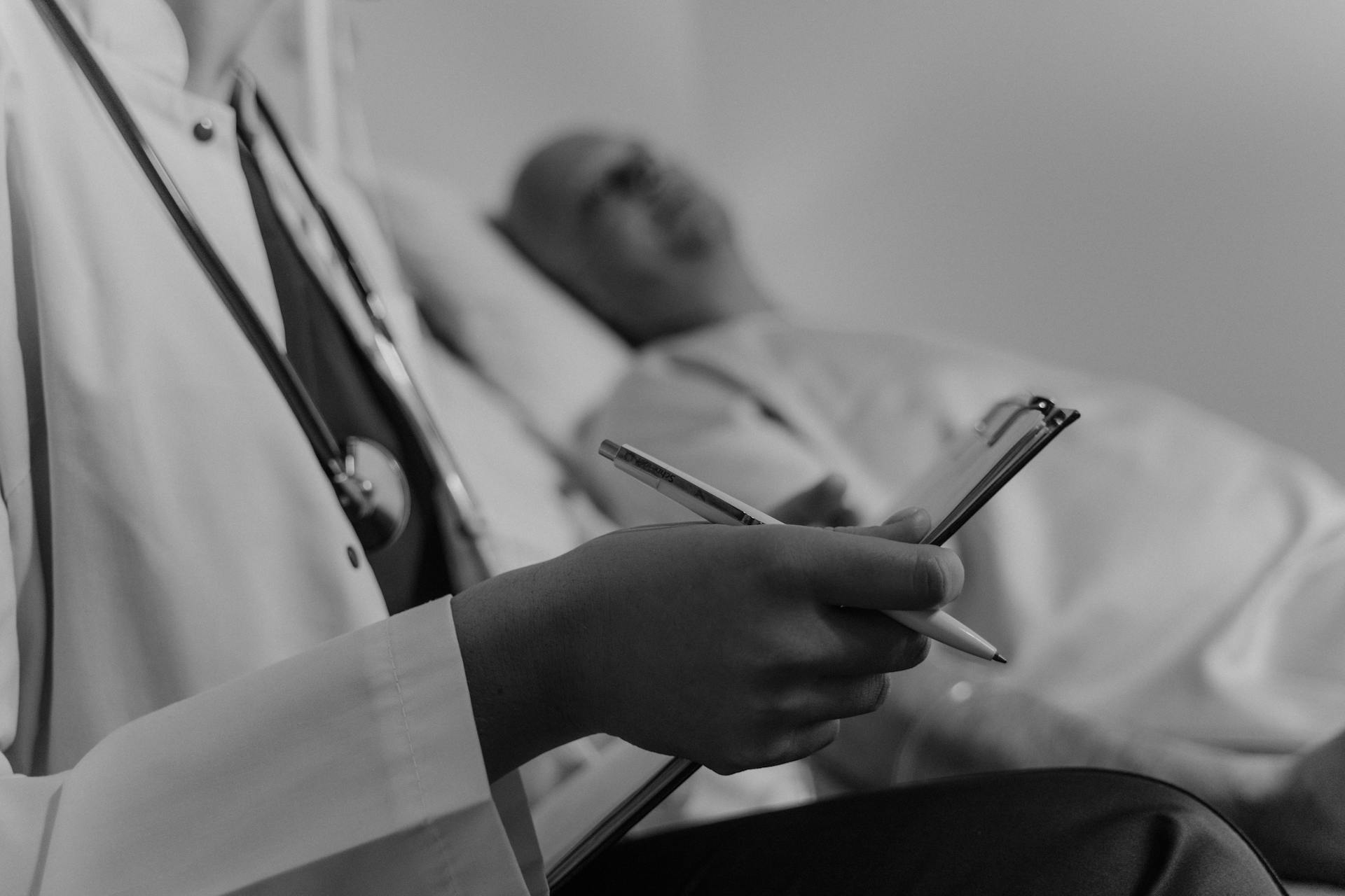 Photo en niveaux de gris d'un médecin tenant un dossier médical tout en se tenant à côté d'un patient | Source : Pexels