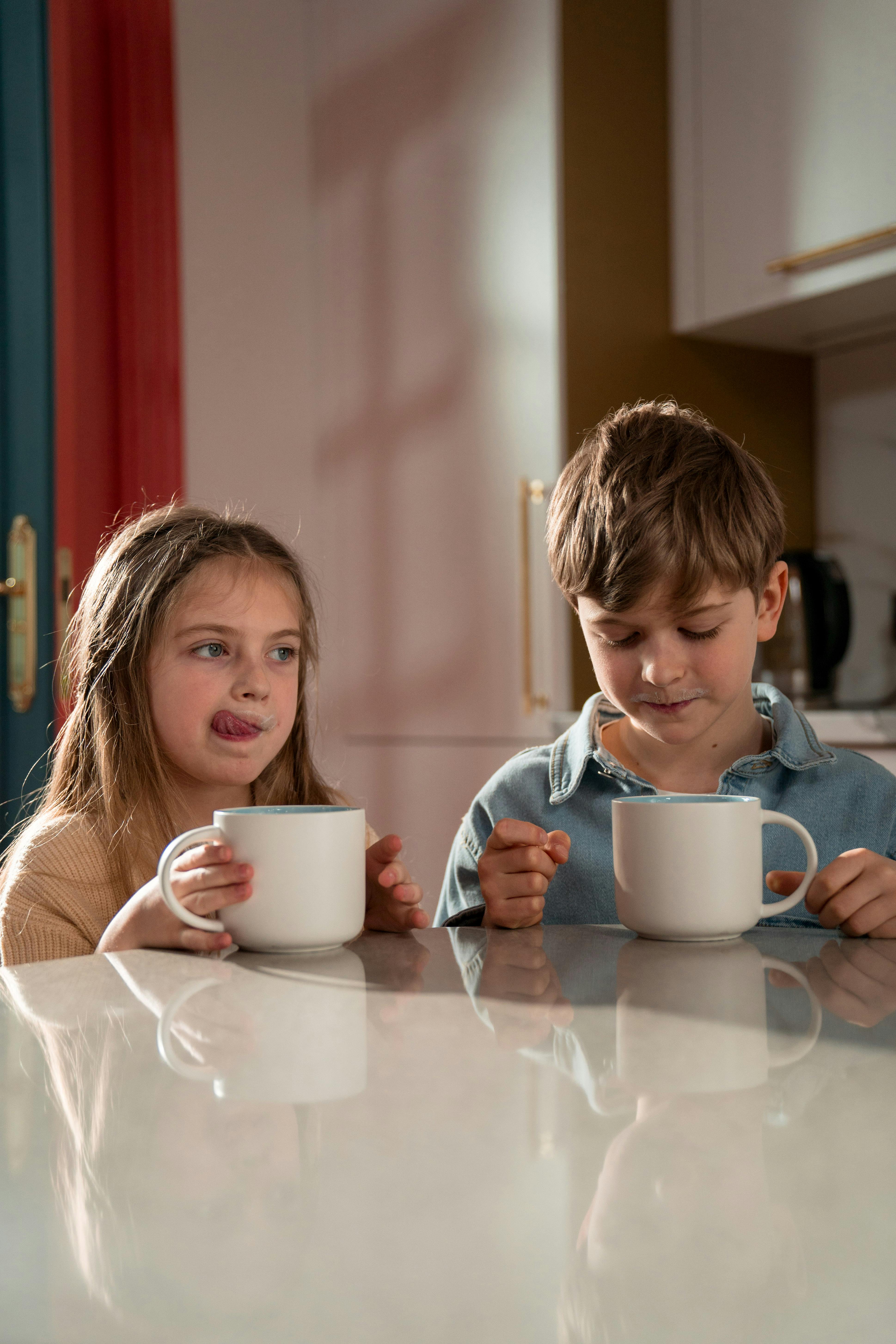 Deux enfants assis à table et dégustant leurs boissons | Source : Pexels