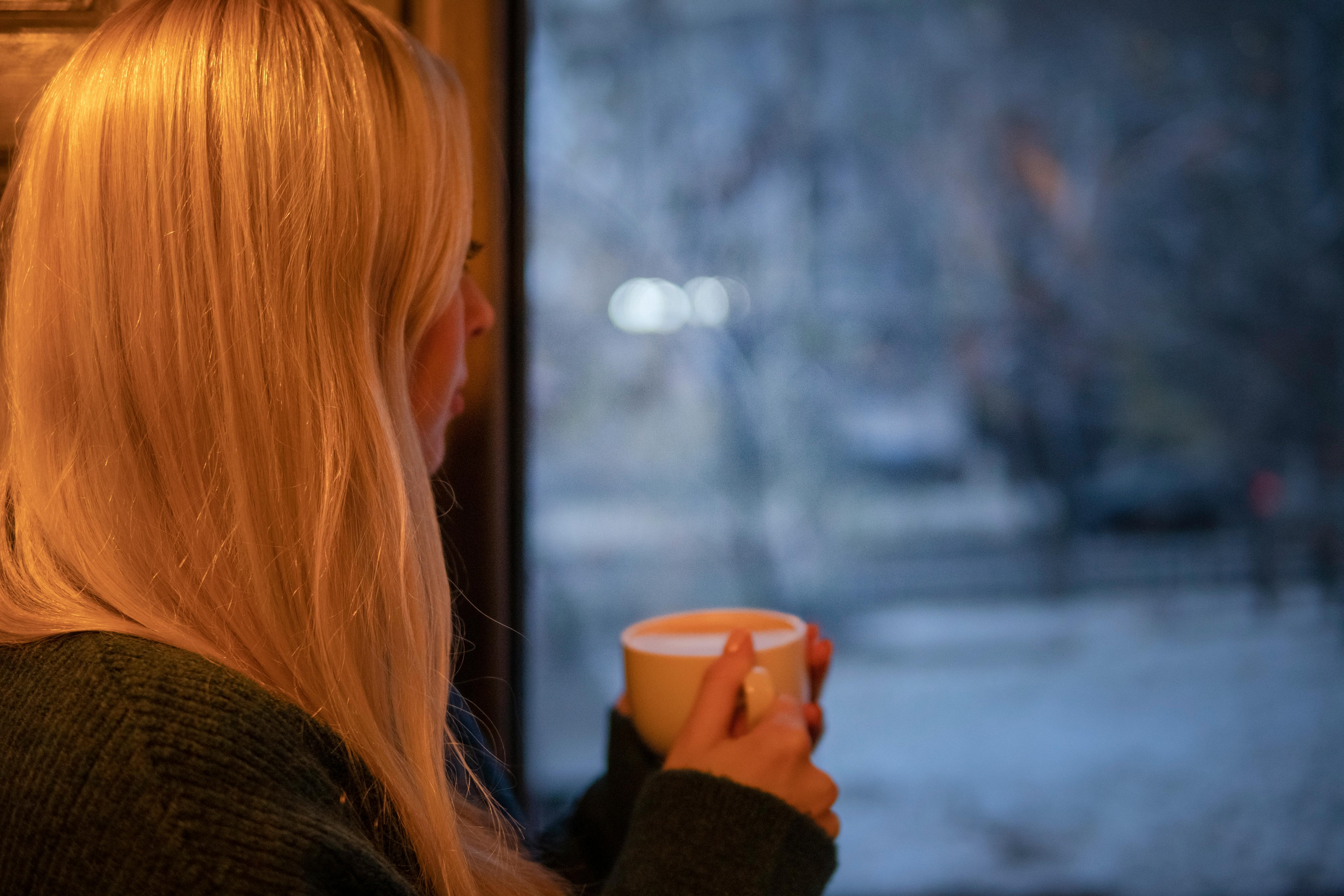 Une fille avec une tasse de café qui regarde par la fenêtre | Source : Pexels