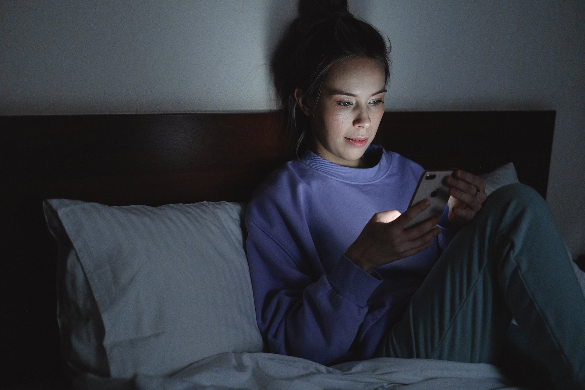 Femme utilisant son téléphone alors qu'elle est assise sur le lit | Source : Pexels