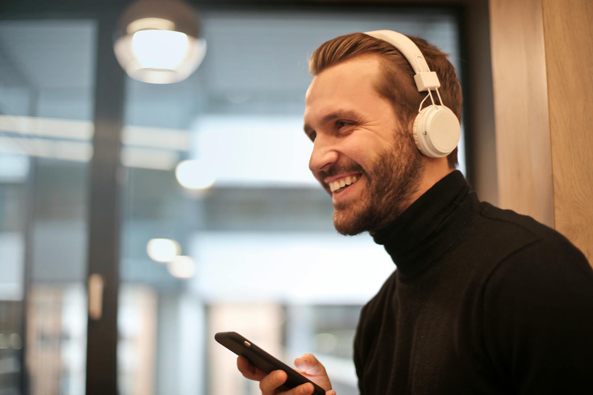 Un homme souriant portant un casque blanc et tenant son téléphone | Source : Pexels