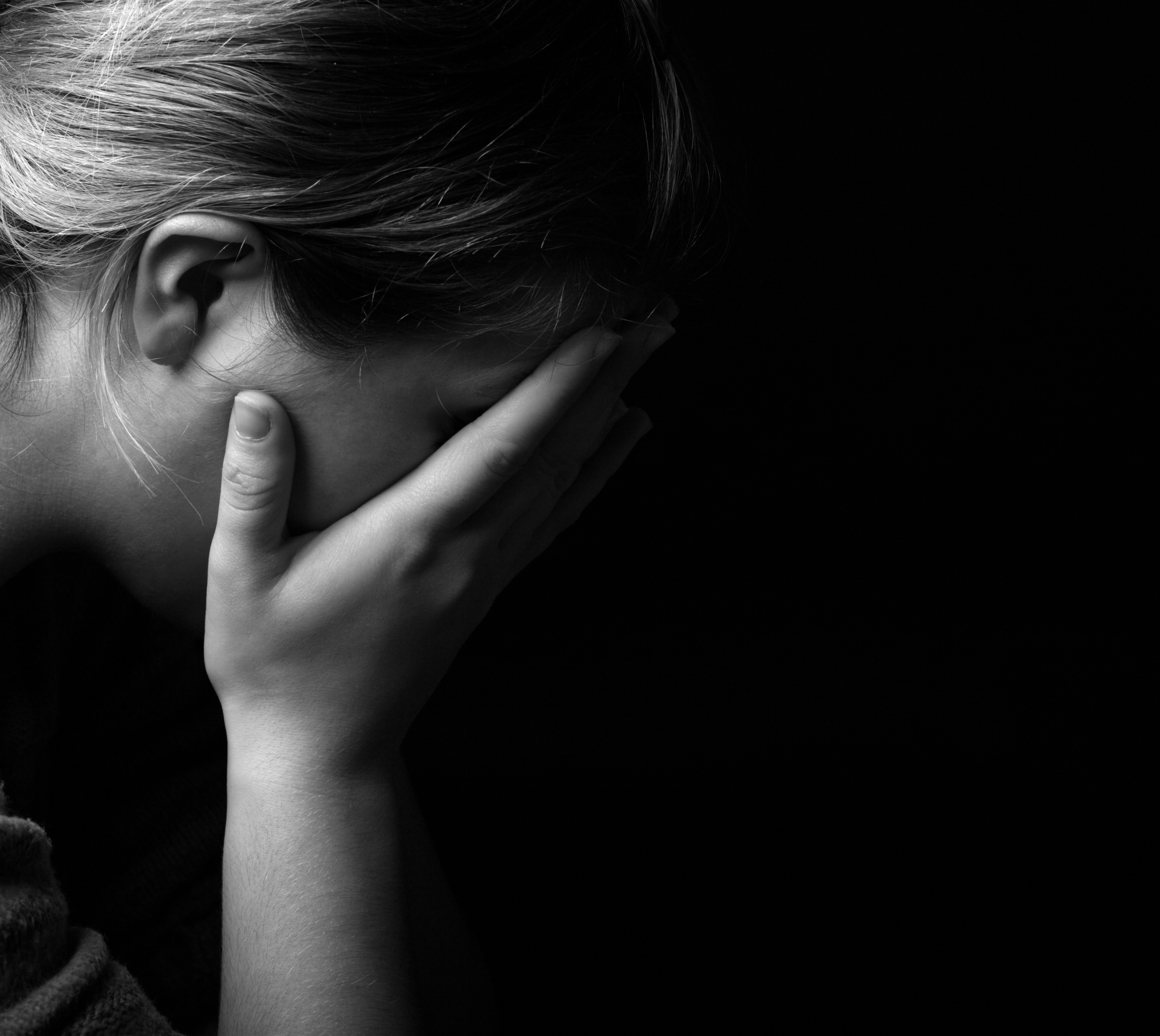 Femme se couvrant le visage de désespoir dans l'obscurité | Source : Shutterstock