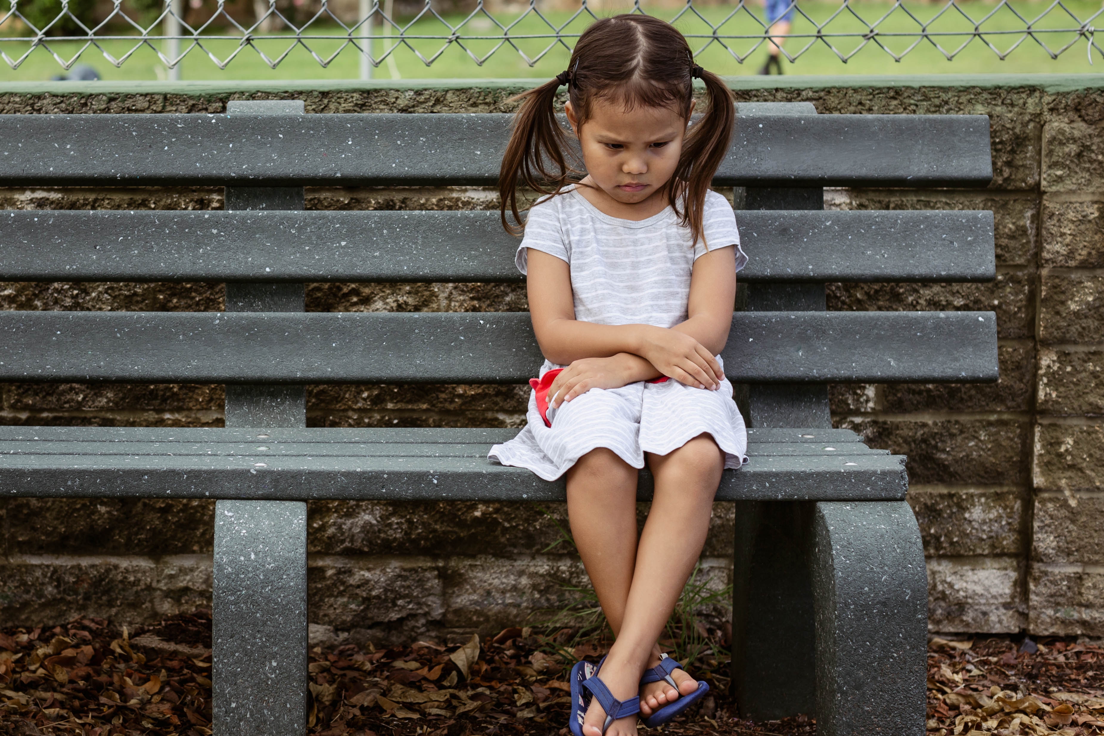 Une petite fille malheureuse assise seule sur un banc | Source : Shutterstock