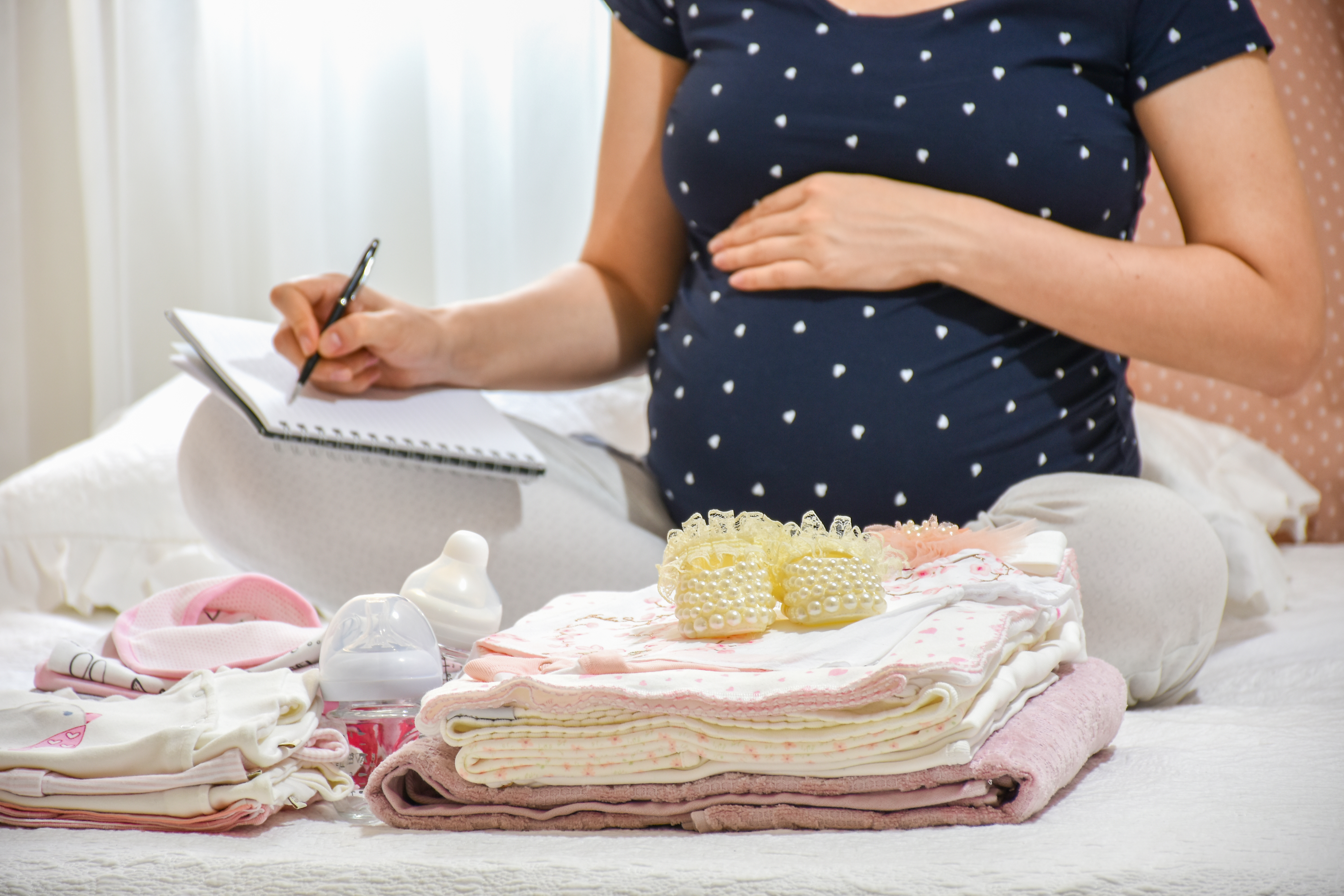 Une femme enceinte avec des vêtements de bébé devant elle | Source : Shutterstock