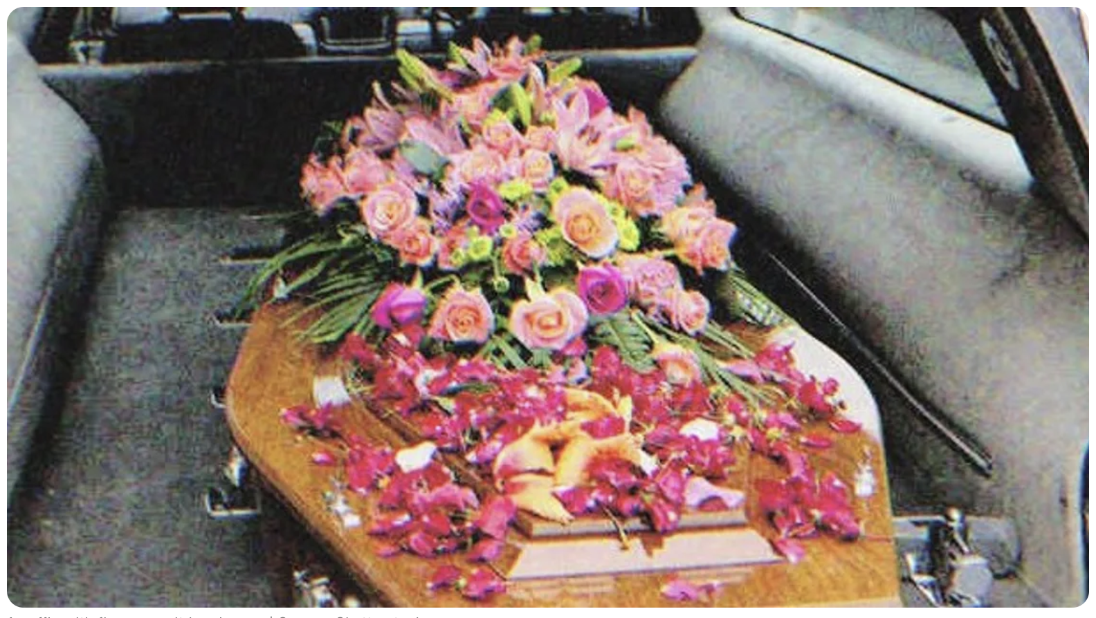 Un cercueil avec des fleurs dessus dans un corbillard | Source : Shutterstock