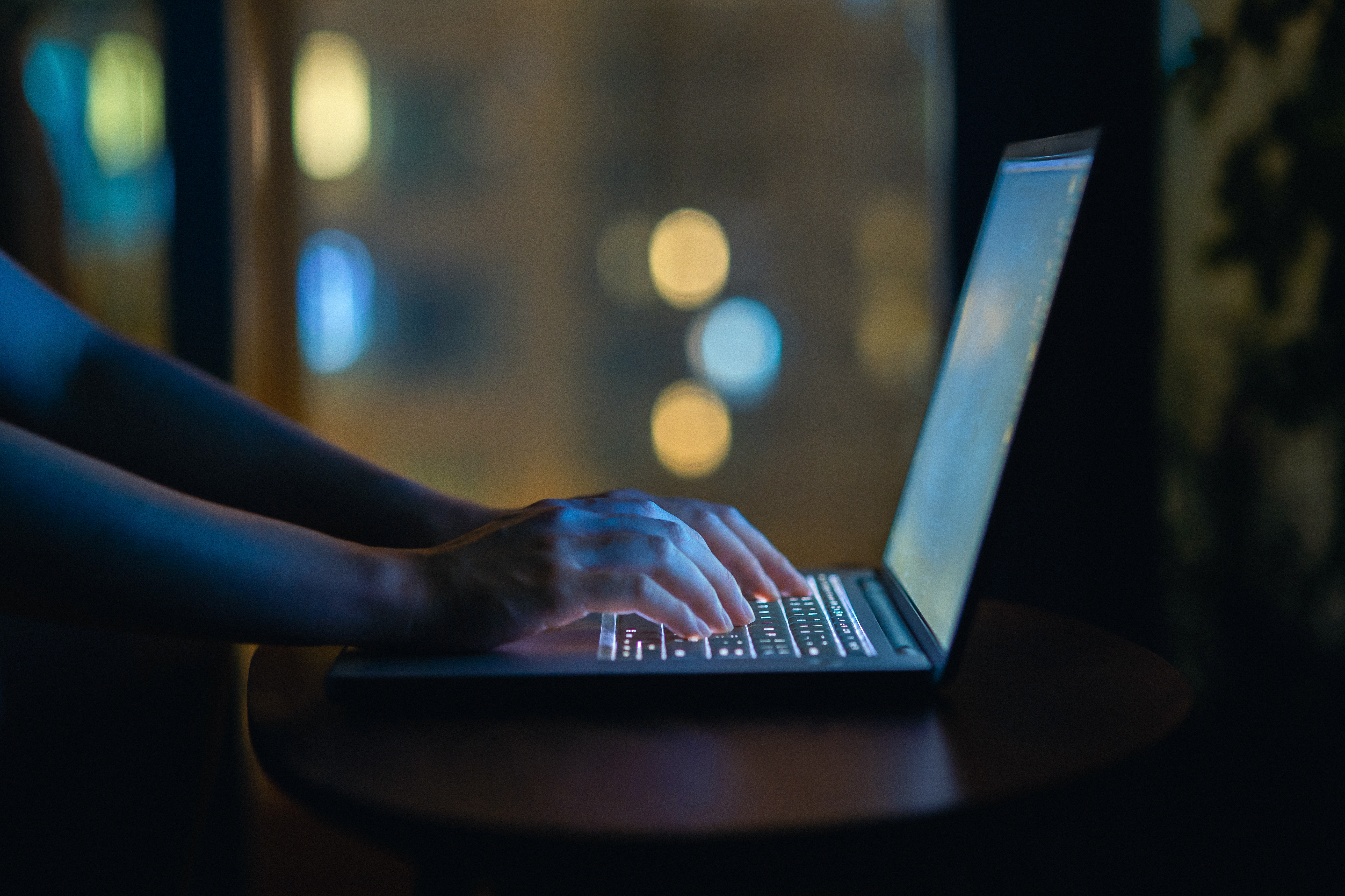 Photo recadrée de la main d'une femme tapant sur un clavier d'ordinateur dans l'obscurité, travaillant tard sur son ordinateur portable à la maison | Source : Getty Images