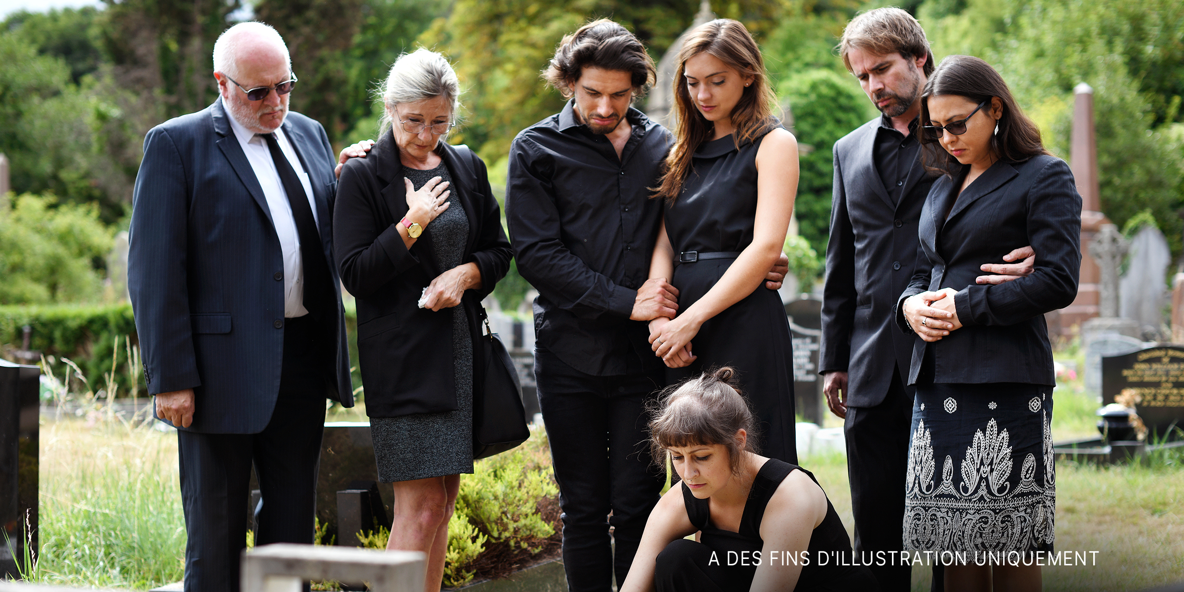 Famille déposant des fleurs sur la tombe dans un cimetière | Source : Shutterstock