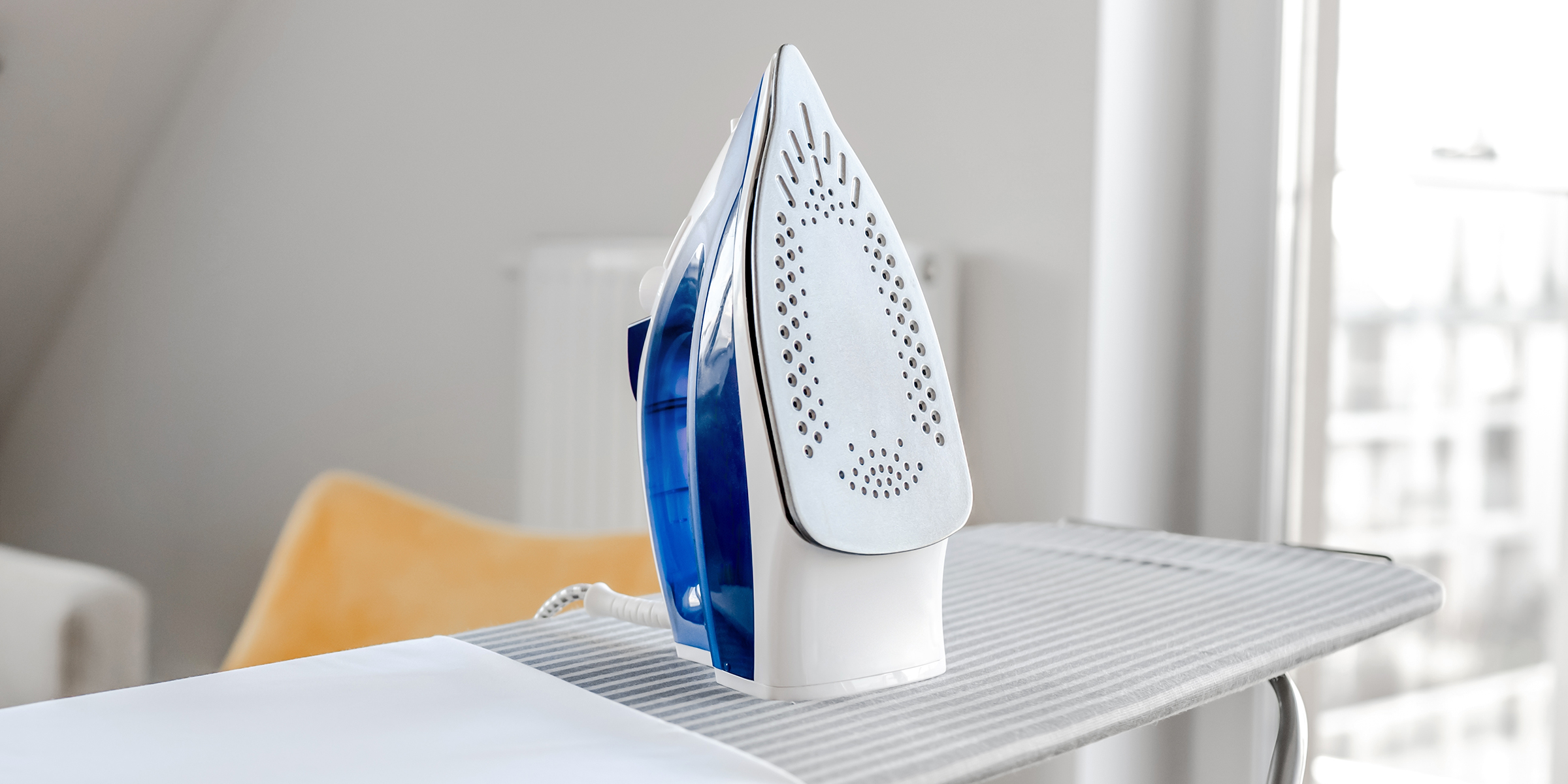 Un fer à vapeur maintenu à la verticale sur une table à repasser dans une pièce lumineuse | Source : Shutterstock