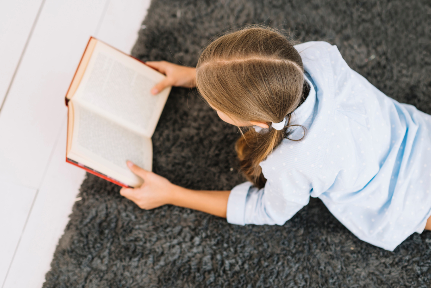 Une fille allongée sur un tapis et lisant un livre | Source : Freepik