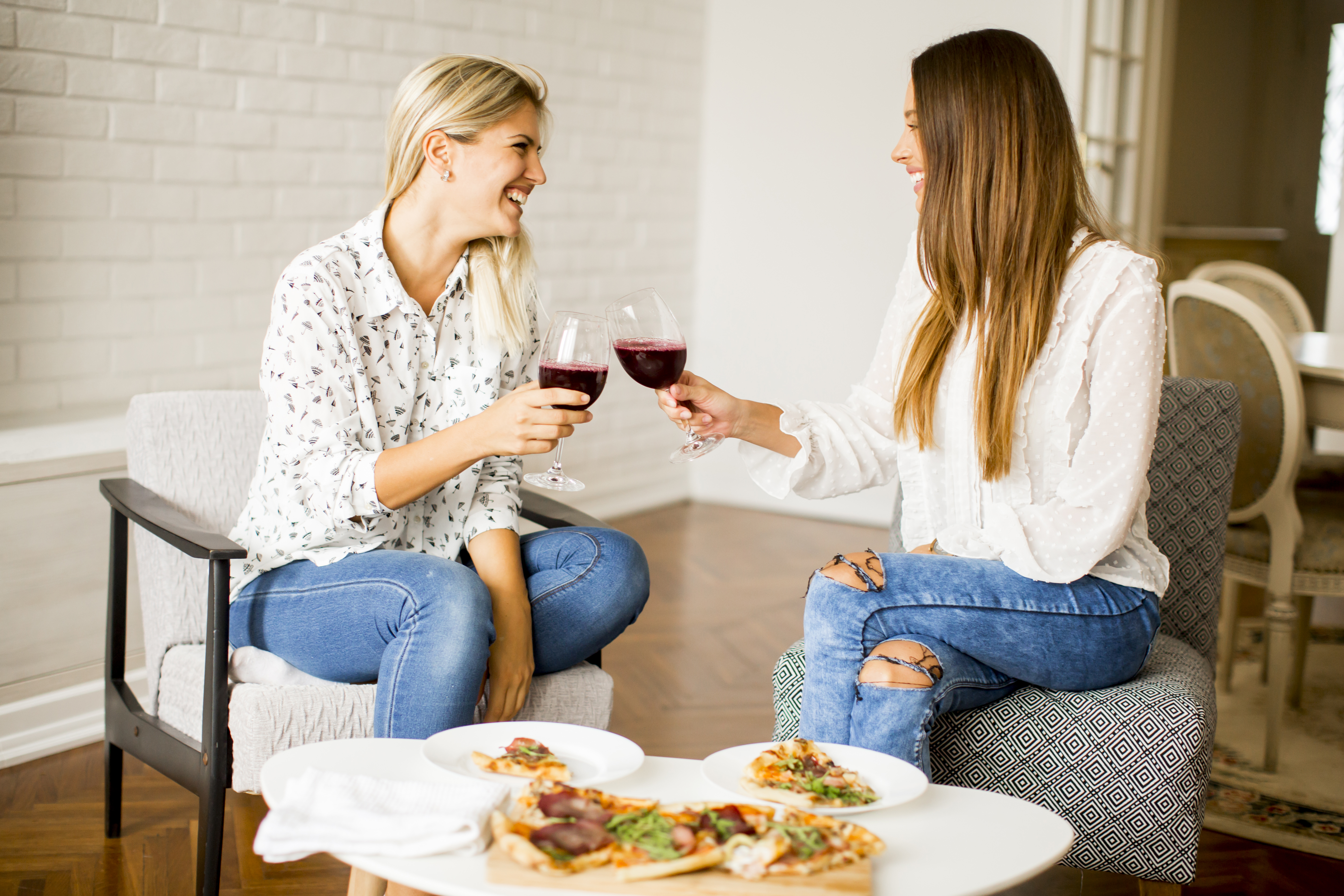 De jolies jeunes femmes mangent de la pizza et boivent du vin rouge | Source : Getty Images