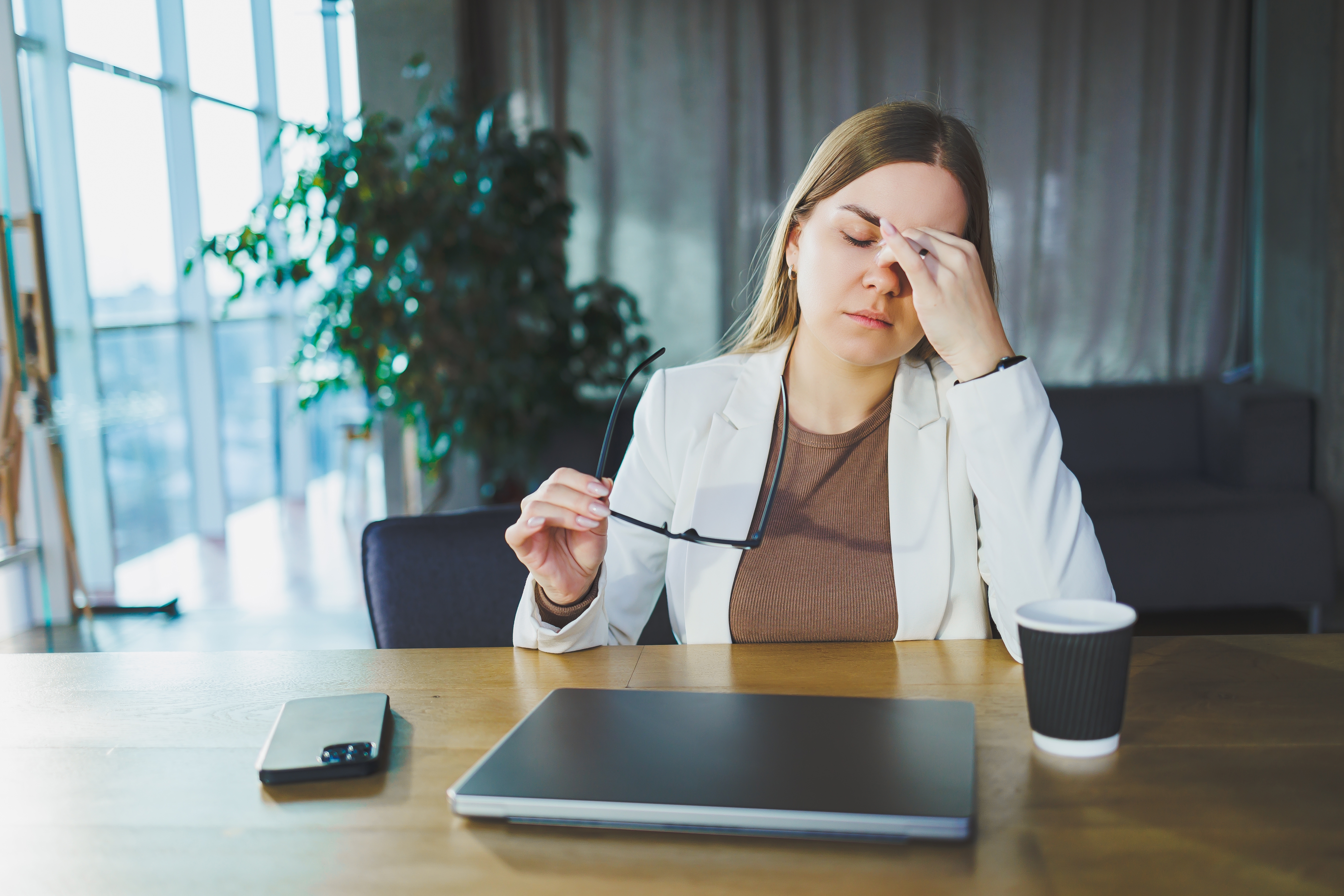 Chica cansada sentada detrás de la mesa con las gafas en los brazos | Fuente: Shutterstock.com