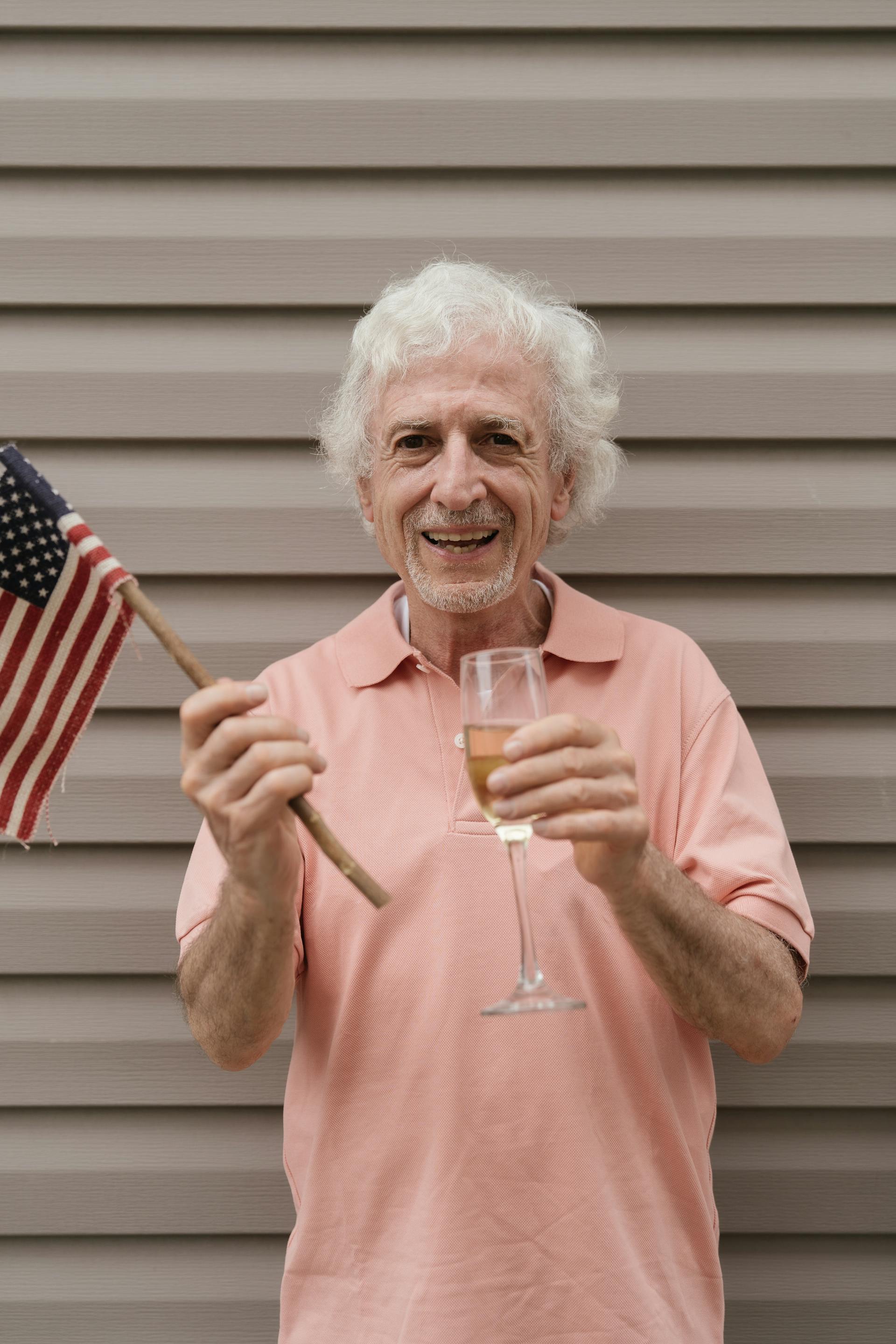 Un homme âgé tenant le drapeau américain et une coupe de champagne | Source : Pexels
