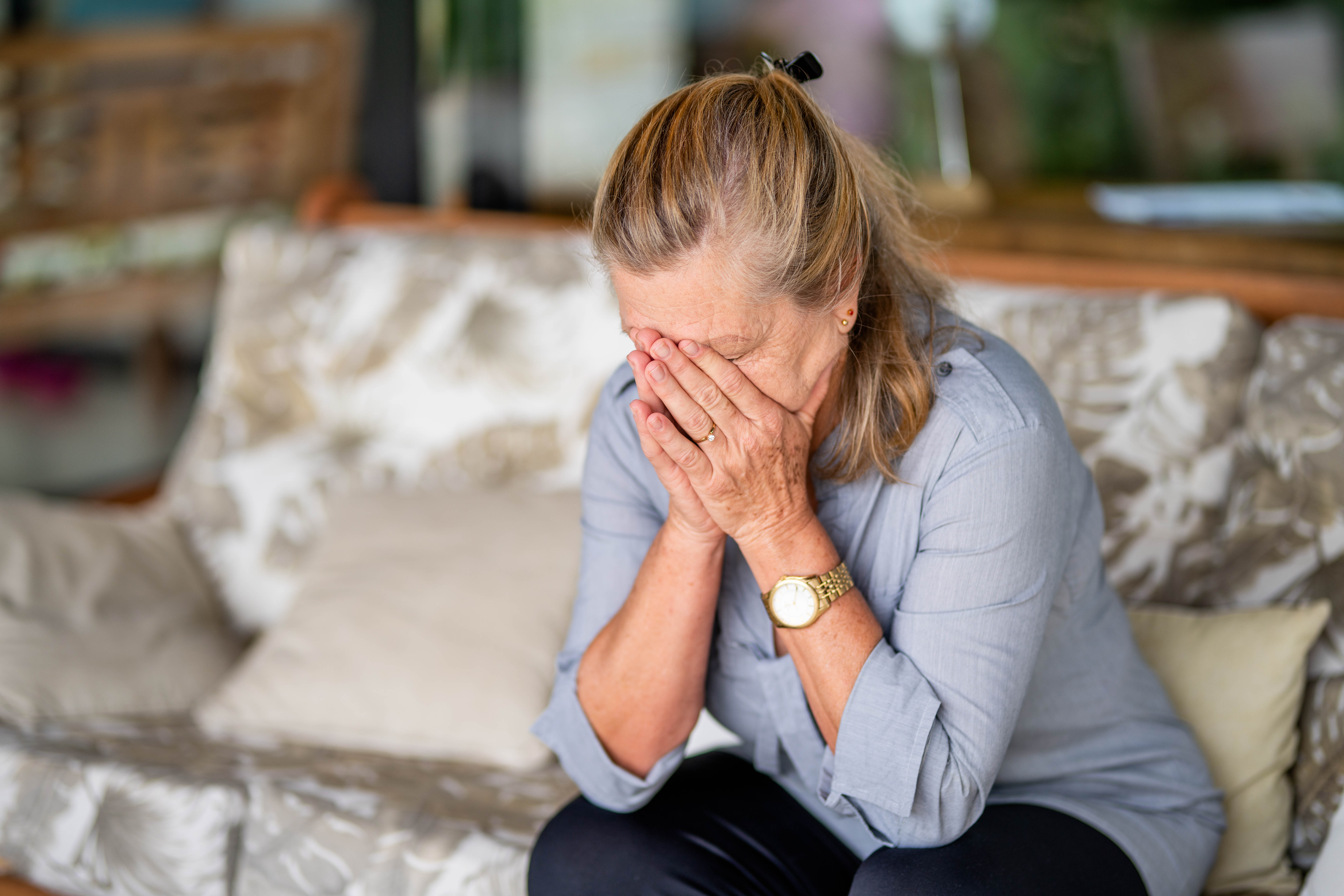 Femme âgée souffrant de dépression, assise, la tête entre les mains, chez elle | Source : Getty Images