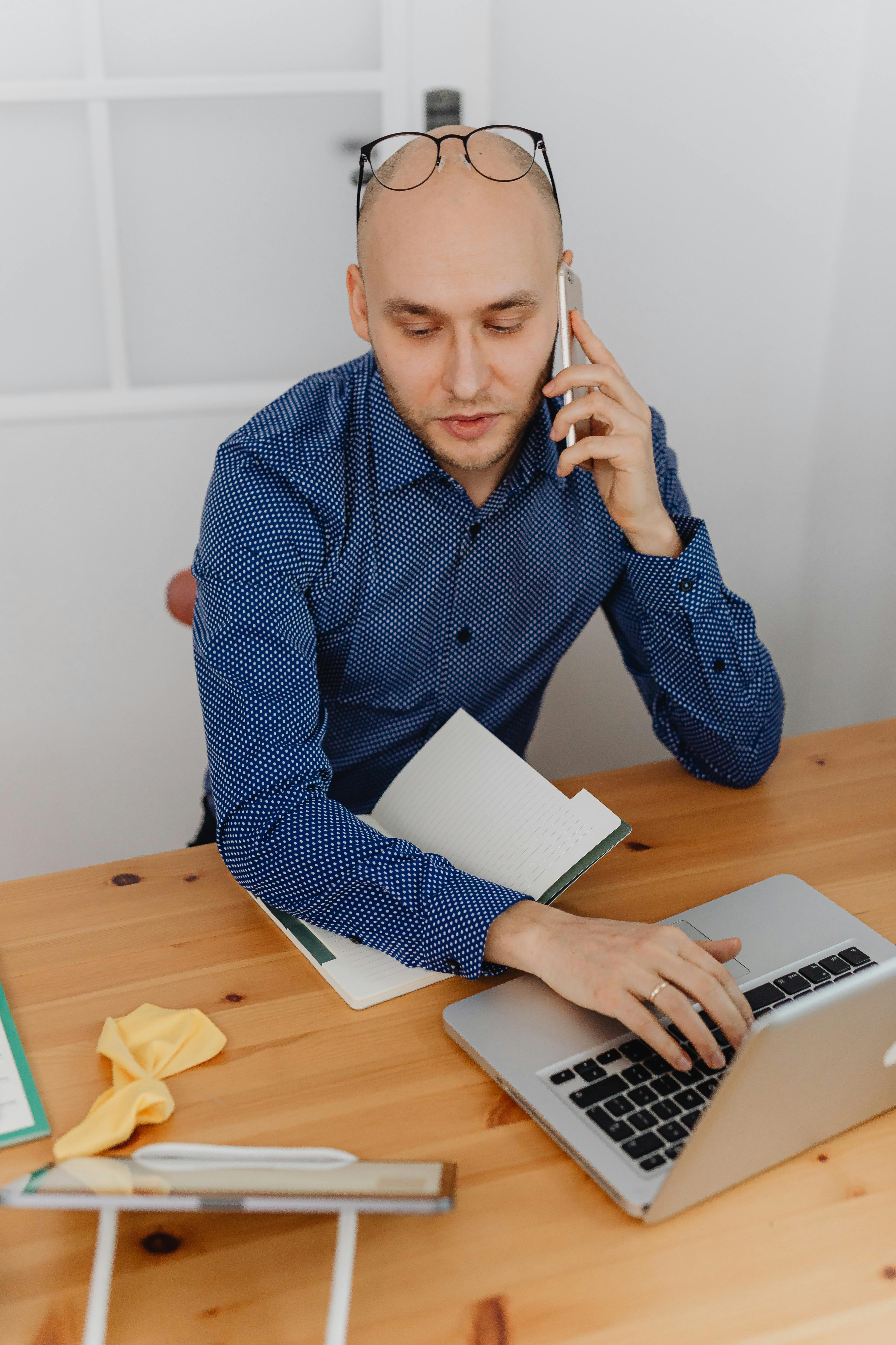 Un homme habillé de façon formelle en train de téléphoner tout en travaillant sur un ordinateur portable | Source : Pexels