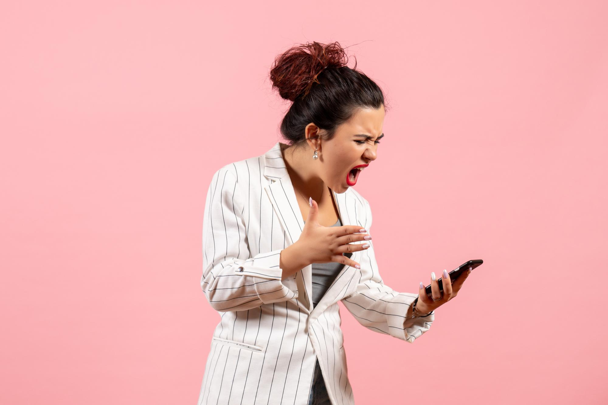 An upset woman reacts badly to something on a phone | Source: Freepik