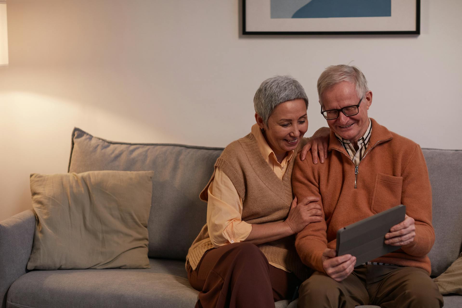 Un homme et une femme âgés sourient en regardant une tablette | Source : Pexels