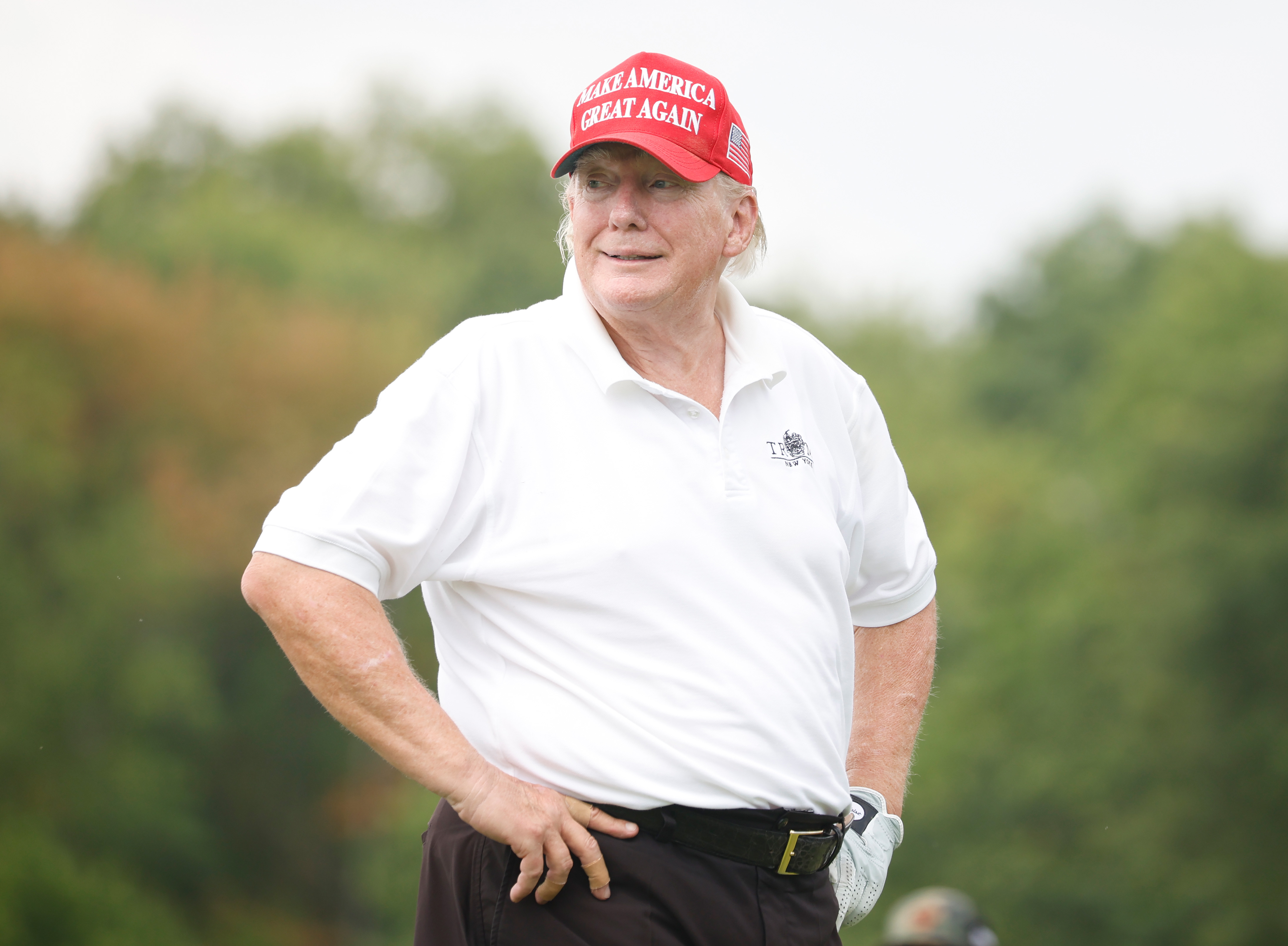 Vêtu de sa casquette rouge et de son polo blanc, Donald Trump se tient sur le terrain de golf, les mains sur les hanches. Ses joues et sa mâchoire sont nettement rouges, ce qui contraste avec la peau pâle de son cou.