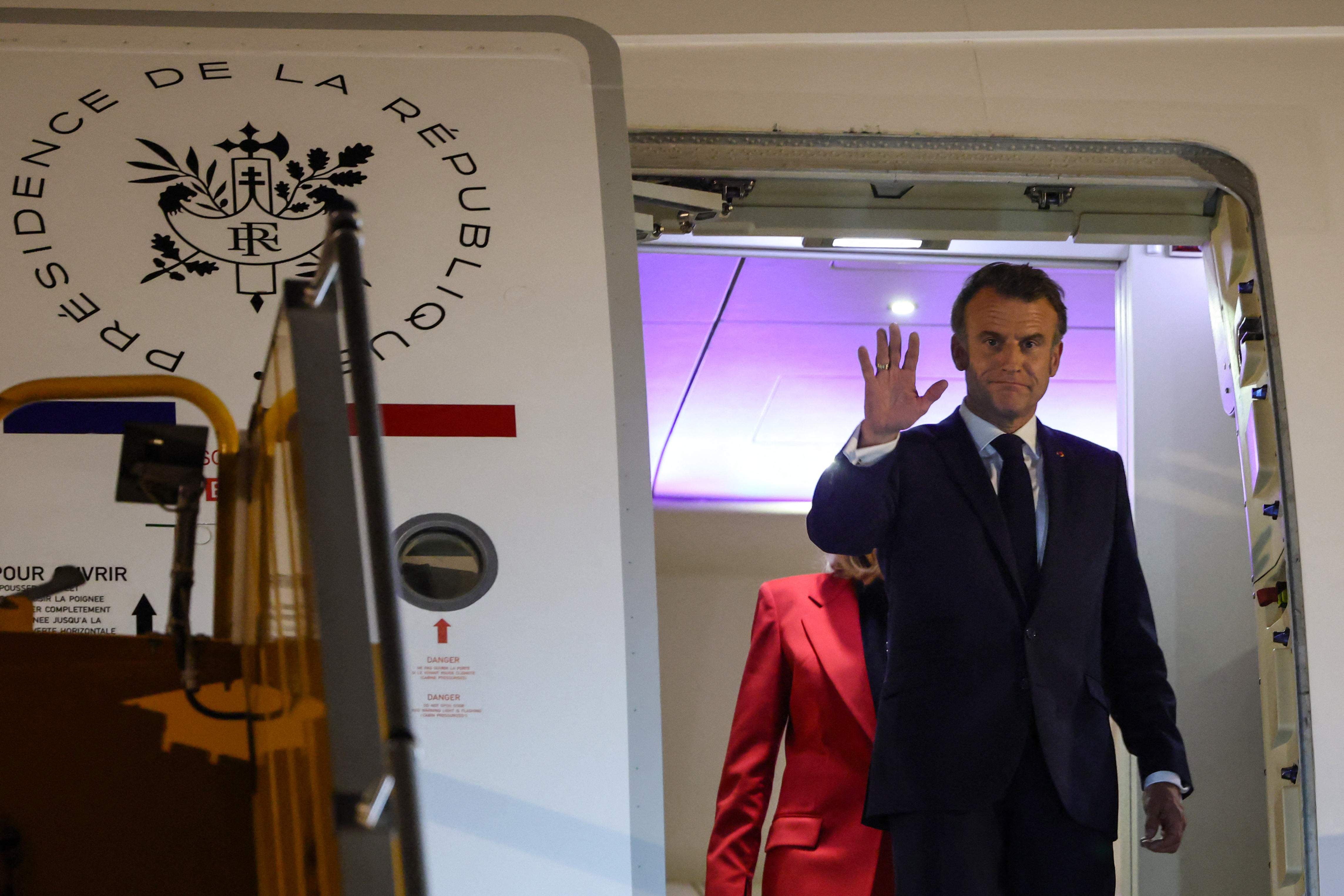 Emmanuel Macron fait un signe de la main alors que Brigitte Macron marche derrière lui. | Source : Getty Images