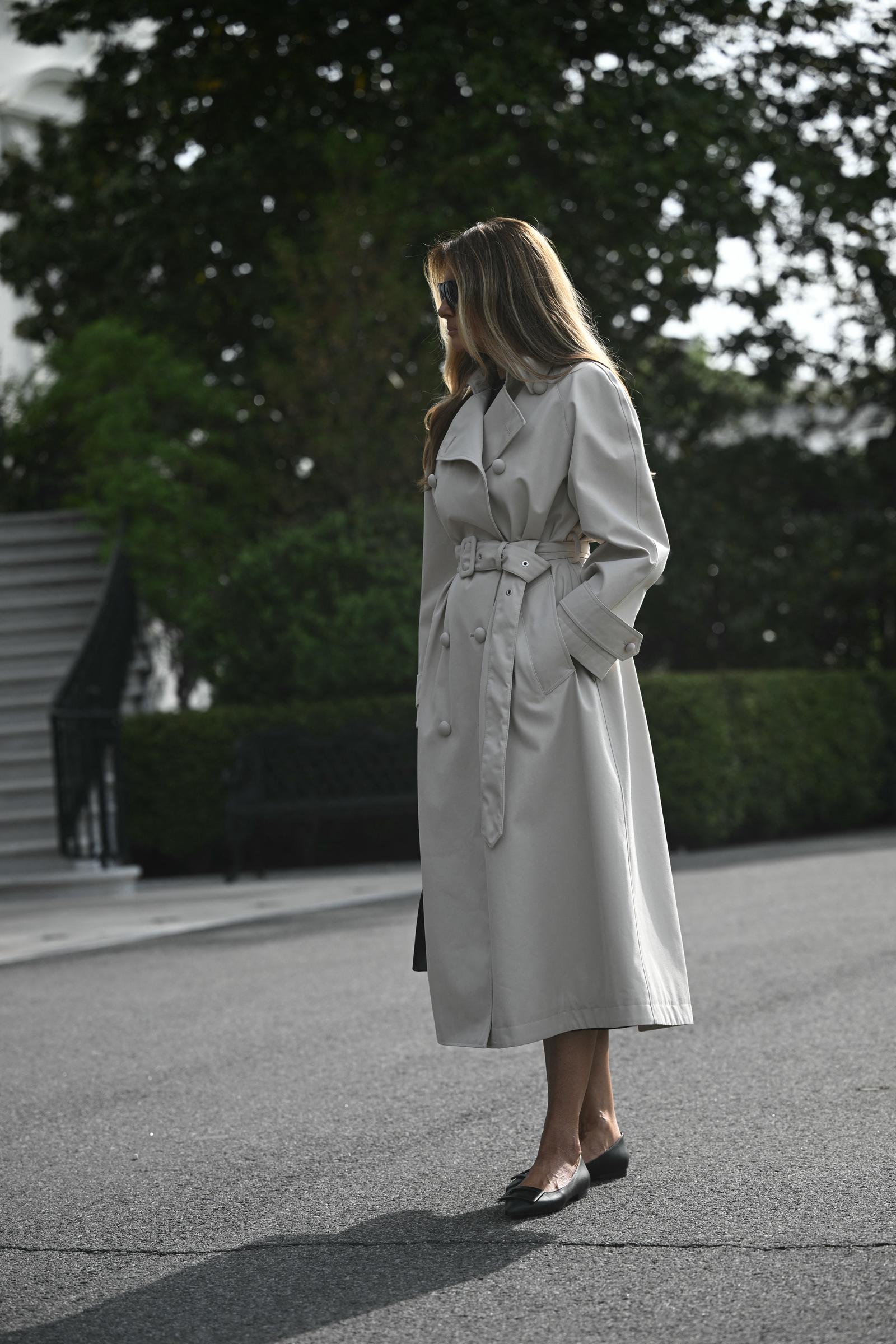 La Première Dame Melania Trump se tient sur la pelouse sud de la Maison Blanche à Washington, D.C., le 25 avril 2025, avant de s'envoler pour la base militaire d'Andrews, en route pour Rome. Elle porte un trench-coat couleur pierre à double boutonnage et ceinturé, ainsi que des lunettes de soleil foncées, le tout assorti à des ballerines noires en cuir à bout pointu, sobres et élégantes, qui apportent une touche raffinée et pratique à sa tenue de voyage.