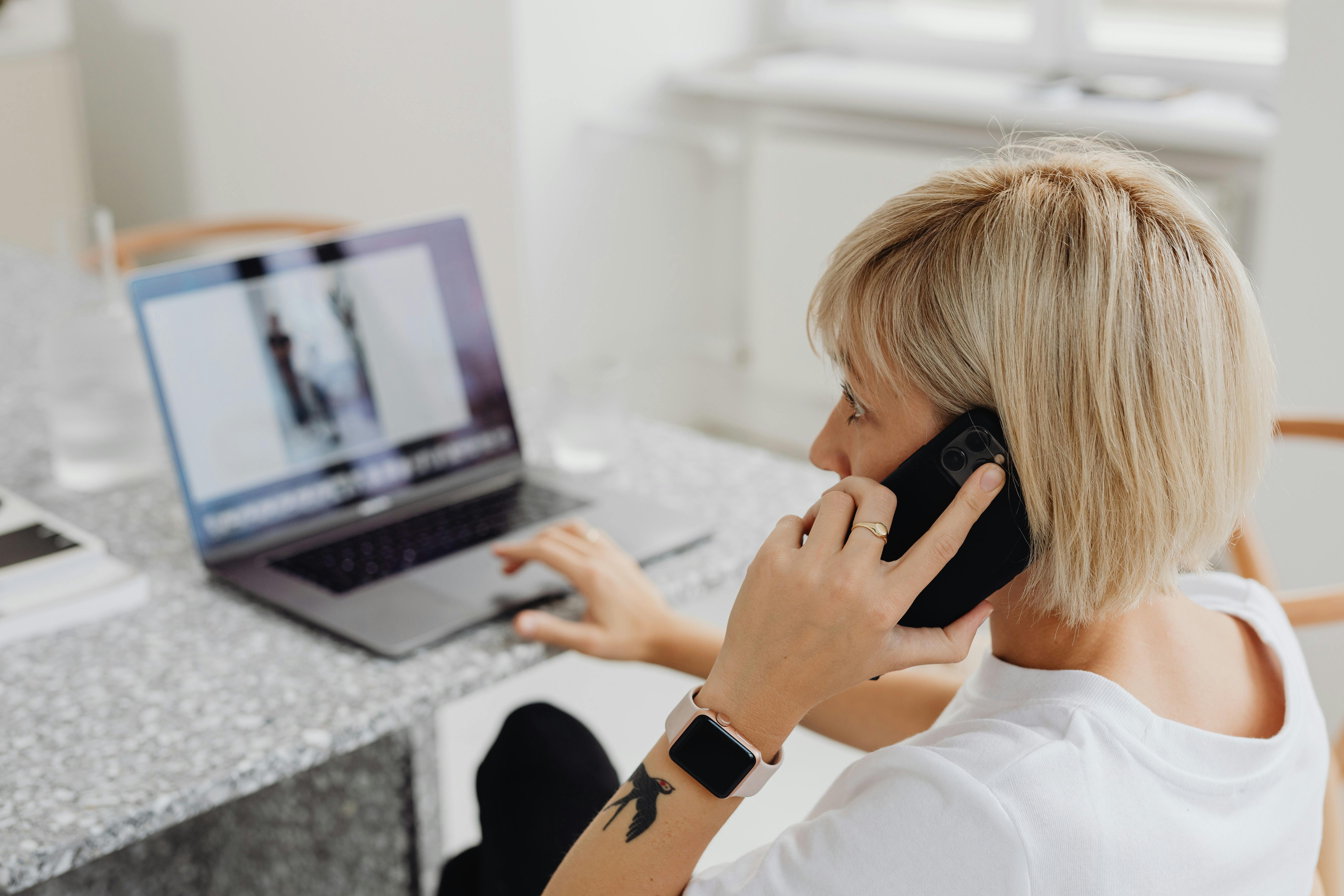 Une femme utilisant un ordinateur portable pendant un appel téléphonique | Source : Pexels