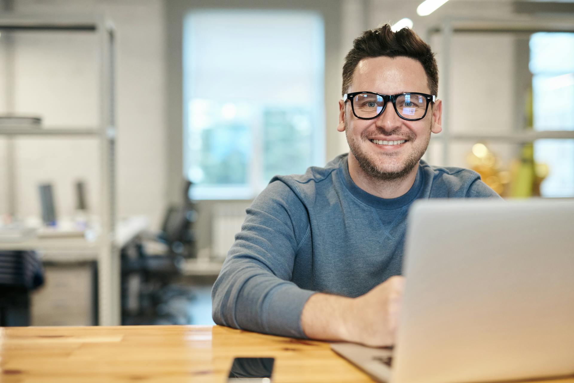 Un homme souriant utilisant un ordinateur portable dans son bureau | Source : Pexels