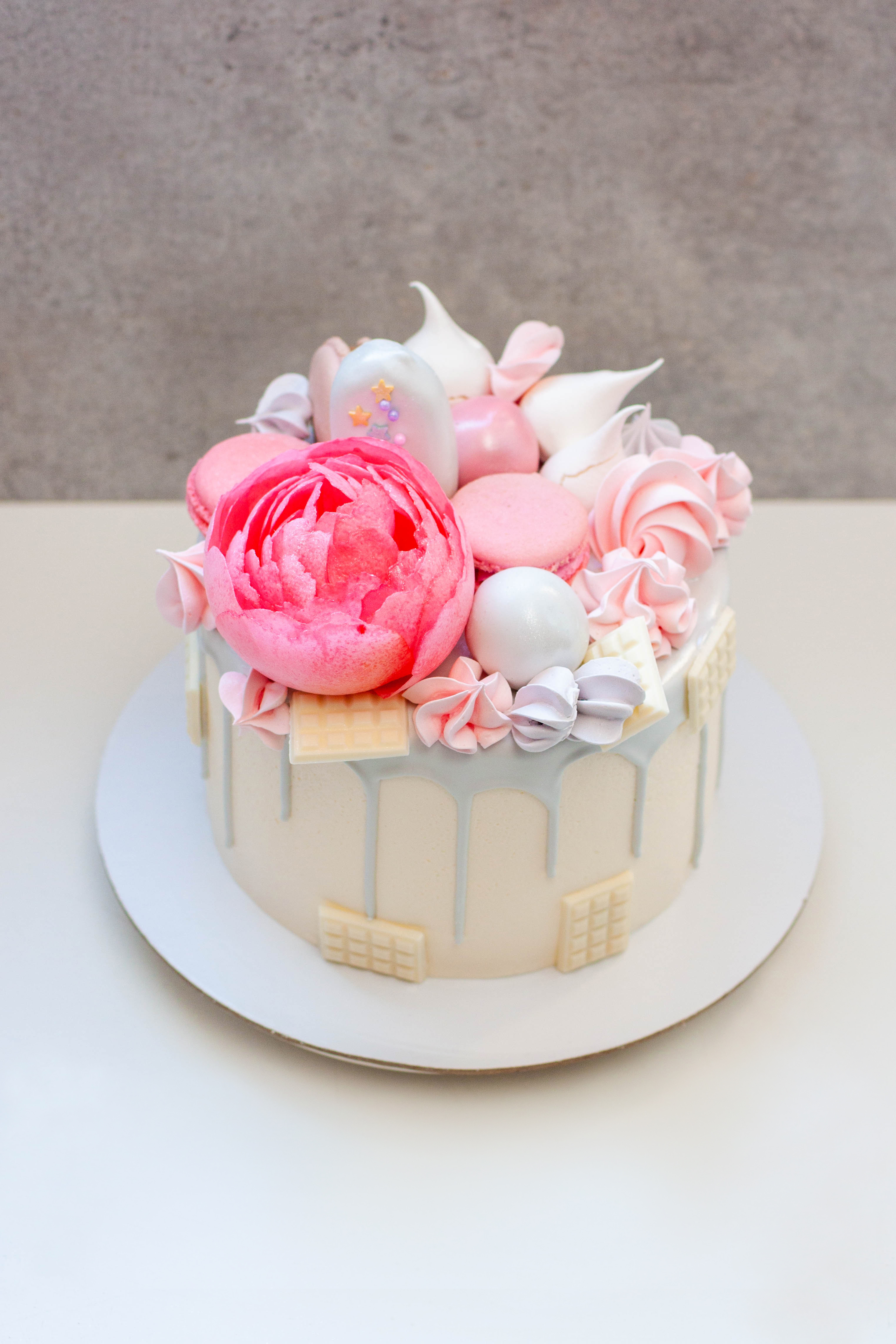 Magnifique et élégant gâteau décoré de chocolat gris fondu, de macarons, d'une fleur de pivoine rose comestible, de bouchées au chocolat et de meringues | Source : Getty Images