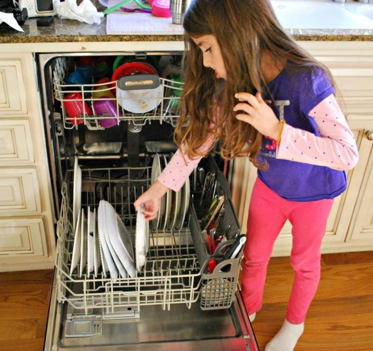 Une petite fille qui range sa vaisselle dans le Lave-vaisselle | Photo : Shutterstock