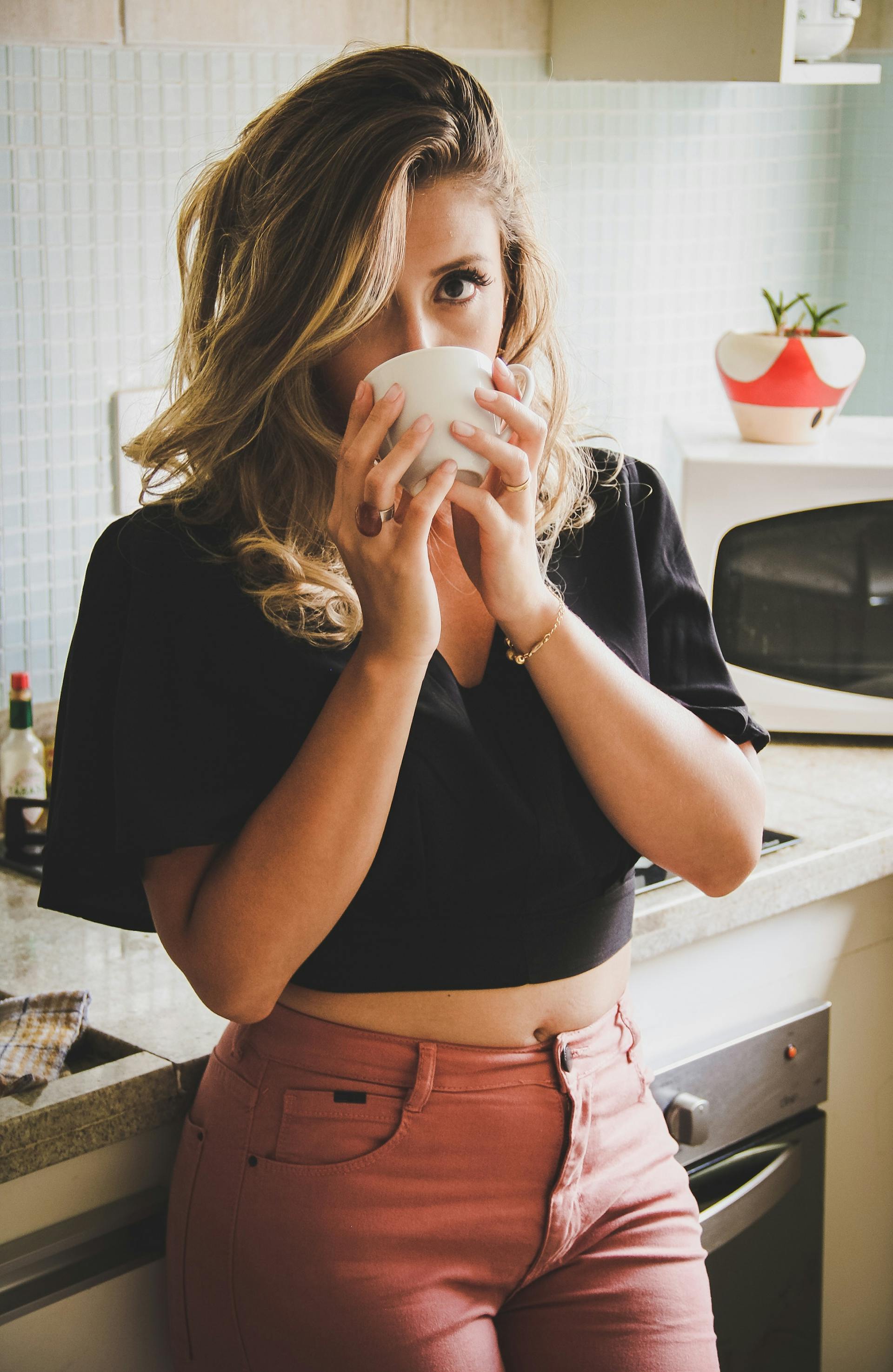 Une femme debout dans une cuisine et buvant dans une tasse | Source : Pexels