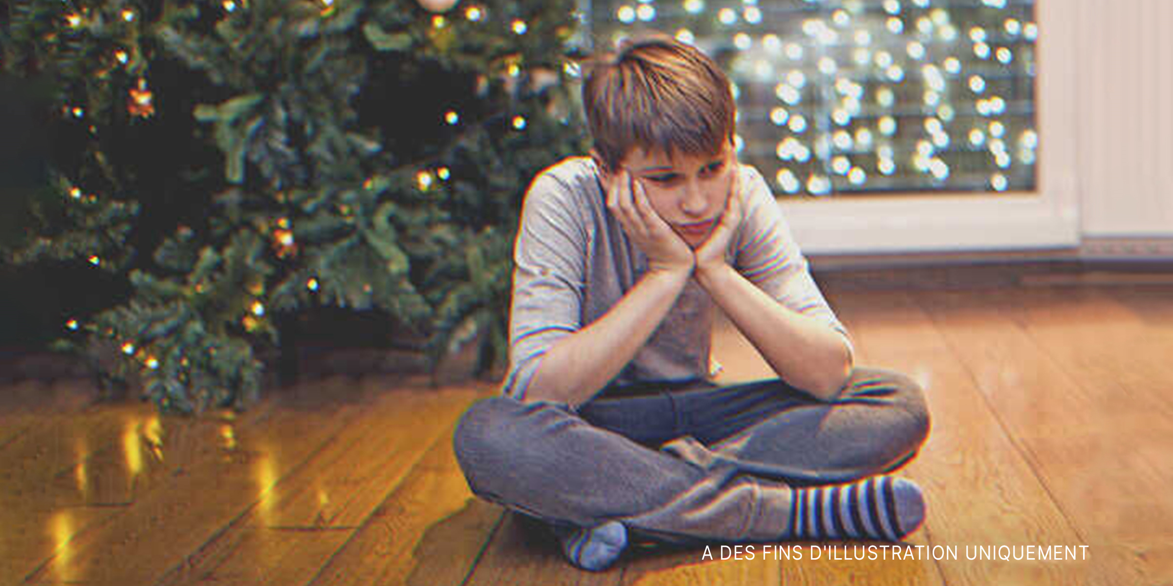 Un garçon assis sur le sol à côté d'un sapin de Noël. | Source : Getty Images