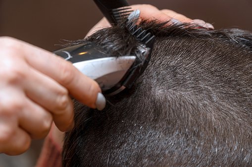 Une coiffeuse coupe les cheveux d'un homme avec une tondeuse électrique. | Photo : Getty Images